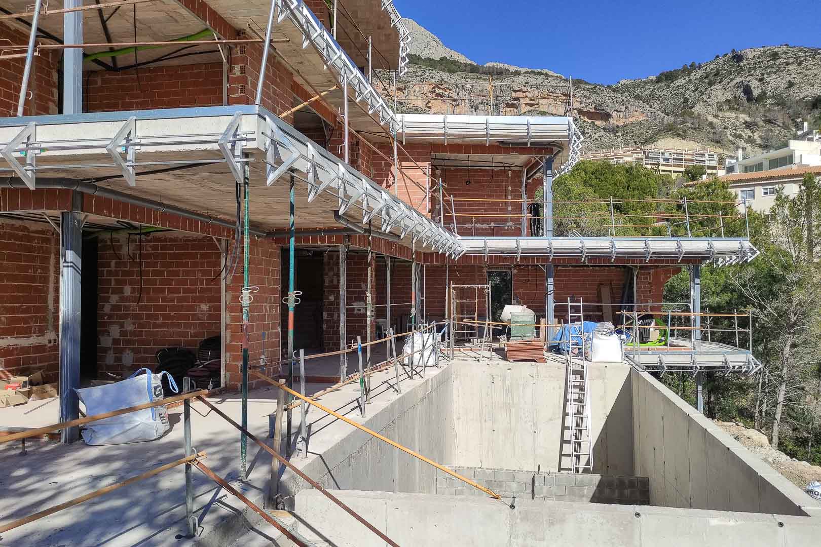 Construction progress of the Altea villa, featuring brick walls, concrete slabs, and the pool shell set against a scenic mountain backdrop.
