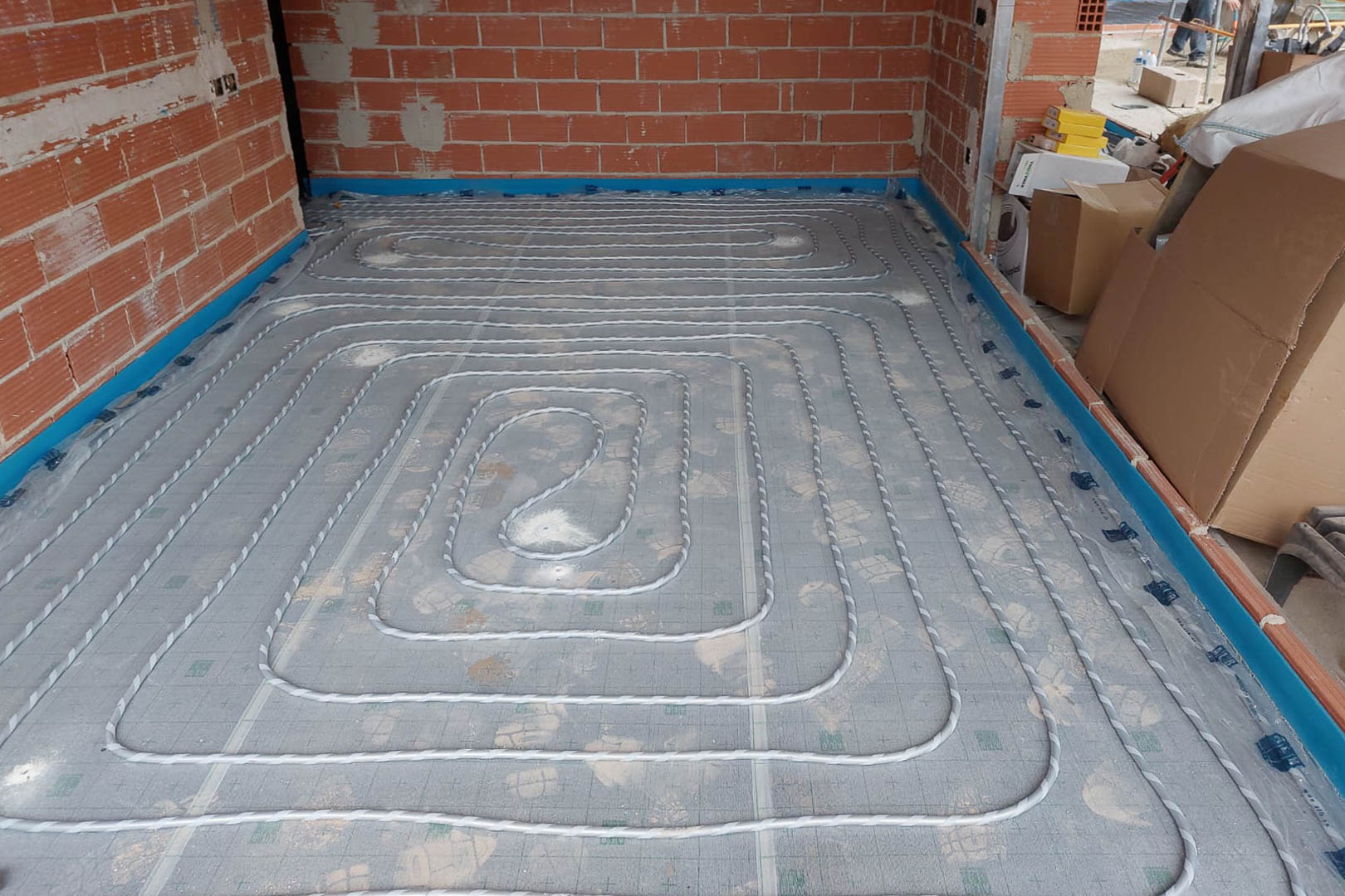 Installation phase of the underfloor heating system featuring coiled piping laid over insulation panels during construction.