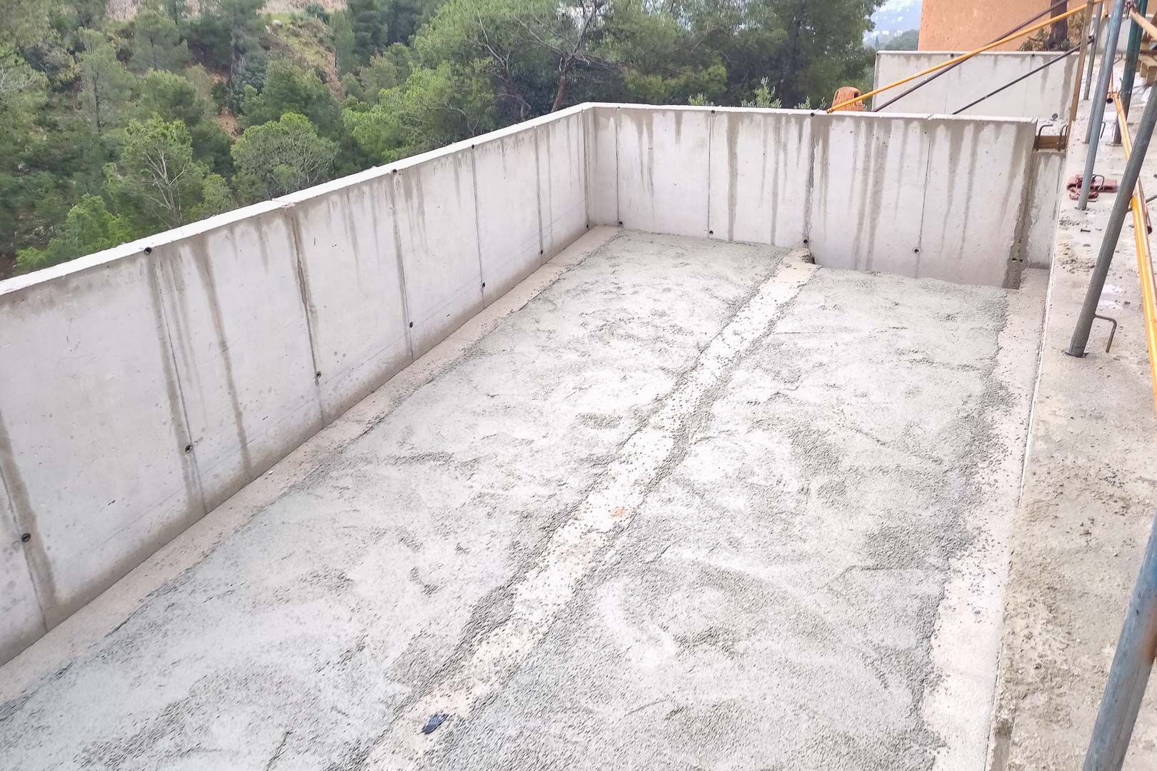 Reinforced concrete structure under construction, featuring perimeter walls and a floor slab for a future terrace overlooking the pine forest.