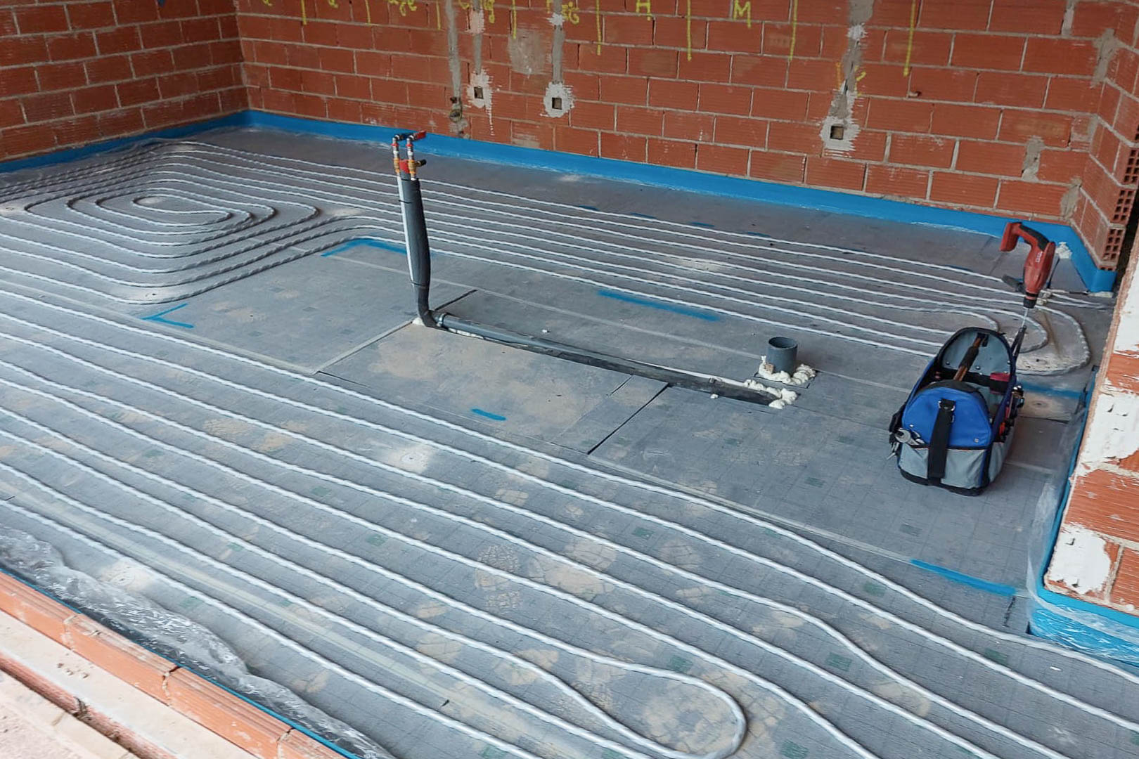 Technical installation of the underfloor heating system, showing the layout of radiant pipes over insulation boards during the structural construction phase.