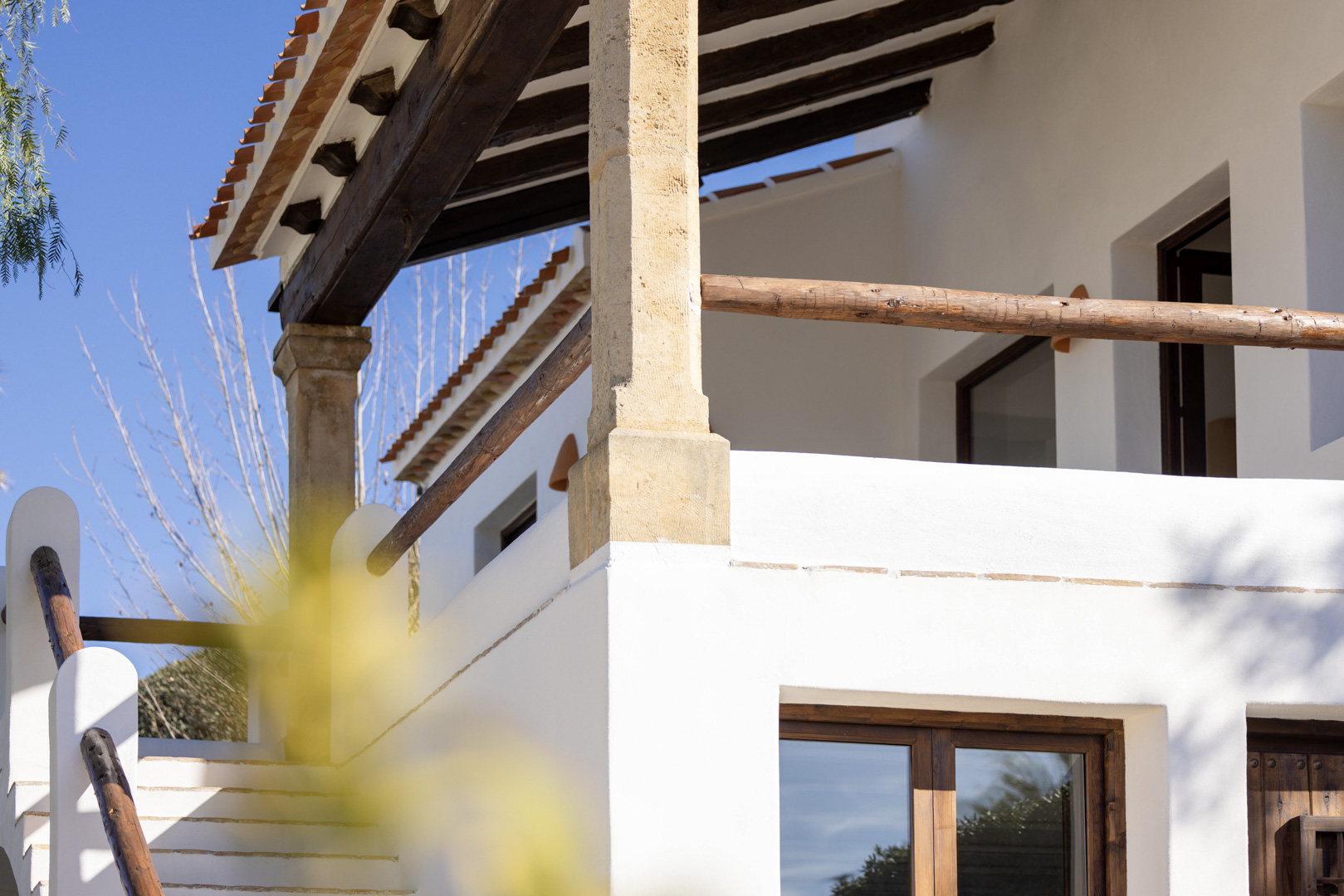Architectural detail of the villa: porch with wooden beams and rustic railing, white stone exterior staircase.
