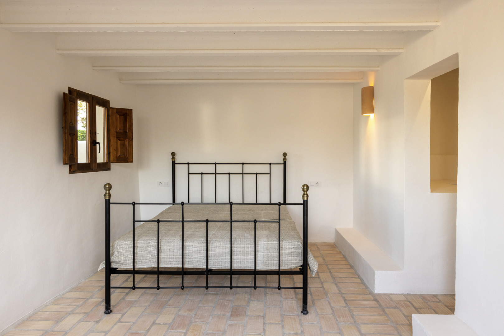 Bright bedroom featuring a wrought iron bed, wooden shutters, and rustic tile flooring.