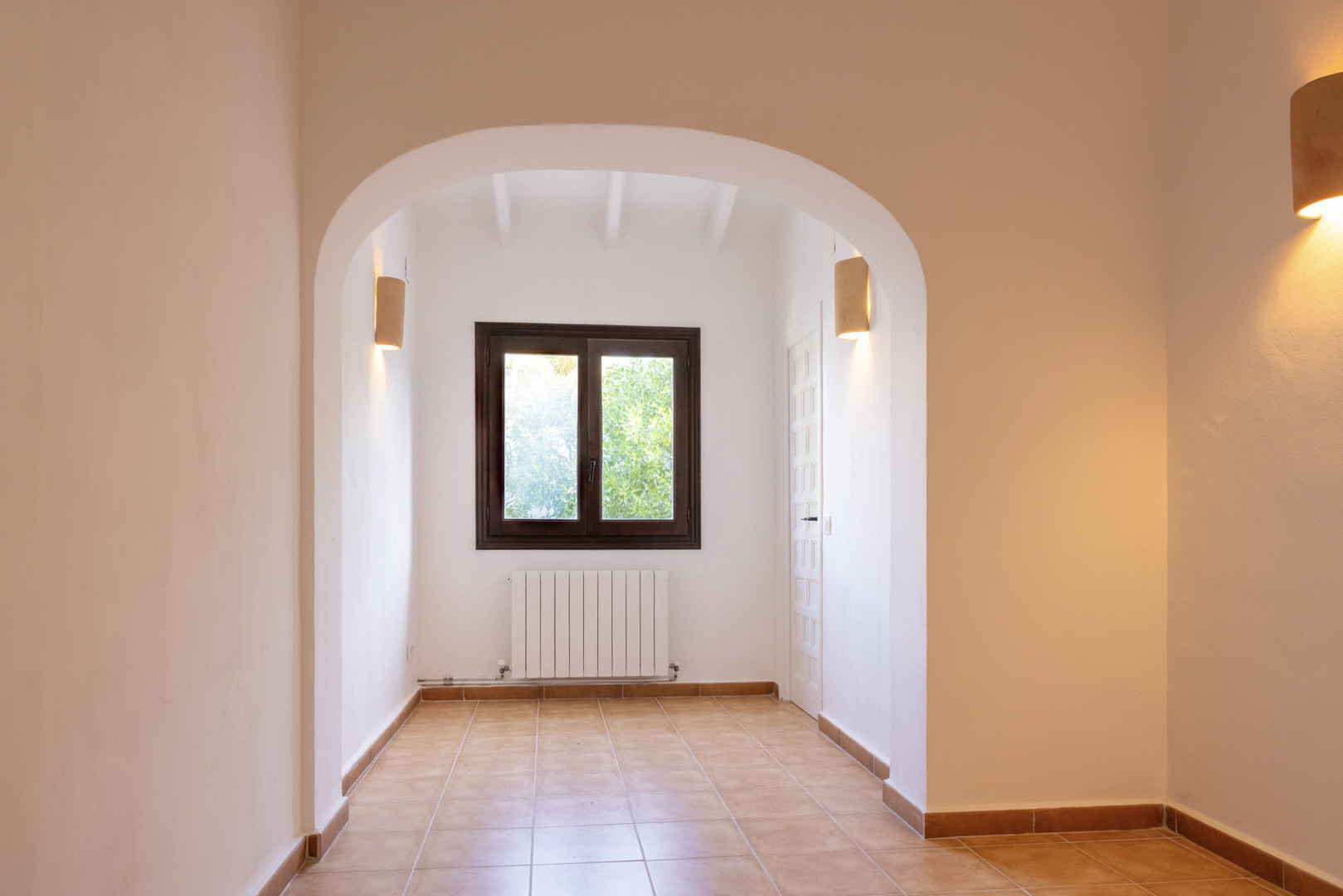 Bright interior featuring an arched entryway, ceramic tile flooring, and a window with dark wood trim.