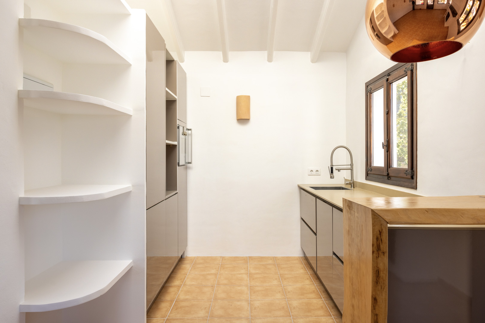 Bright kitchen featuring white built-in shelves, gray cabinets, and a wood countertop. Rustic tile flooring.