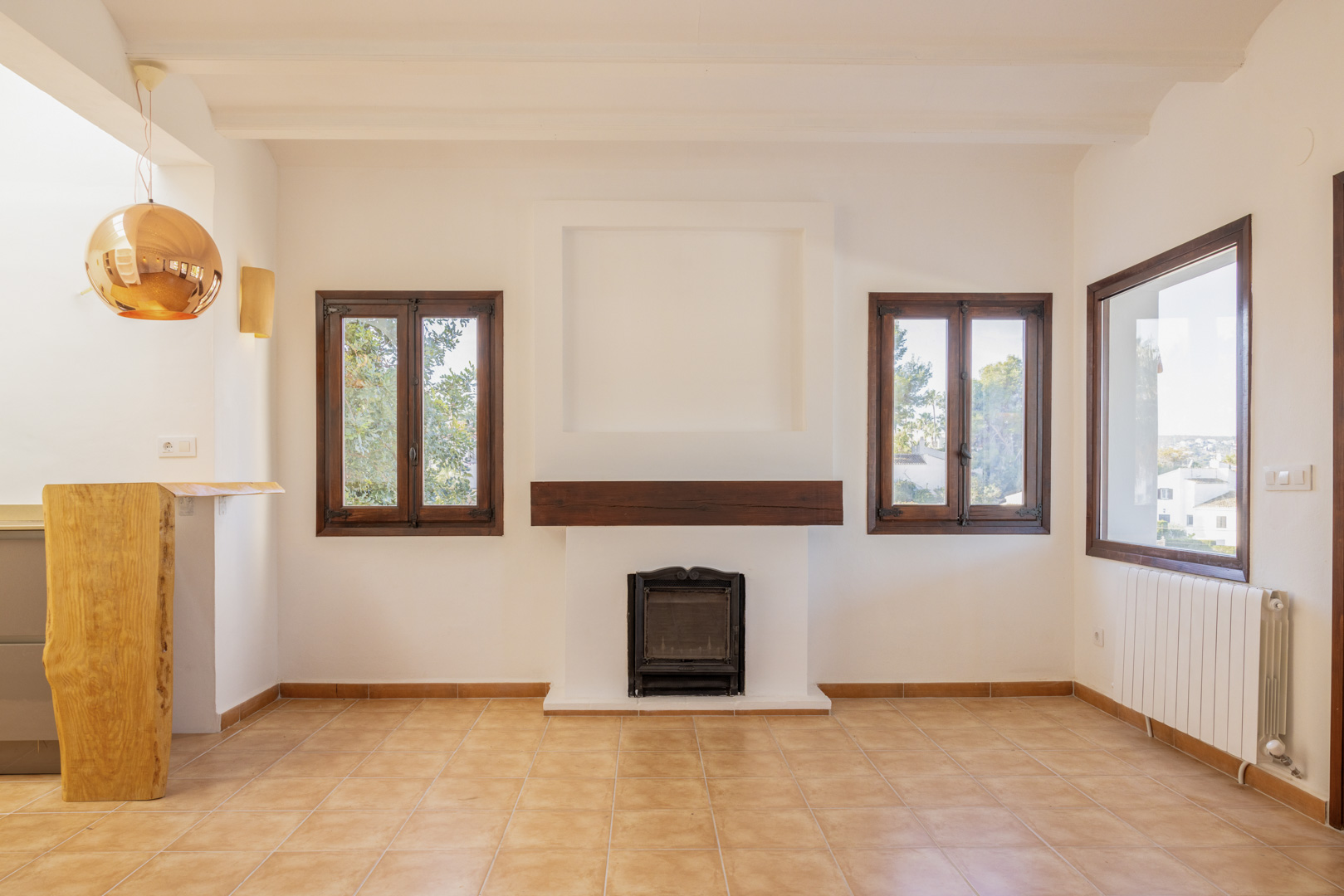 Bright living room with rustic fireplace, wood-framed windows, and tile flooring. Mediterranean design with modern touches.