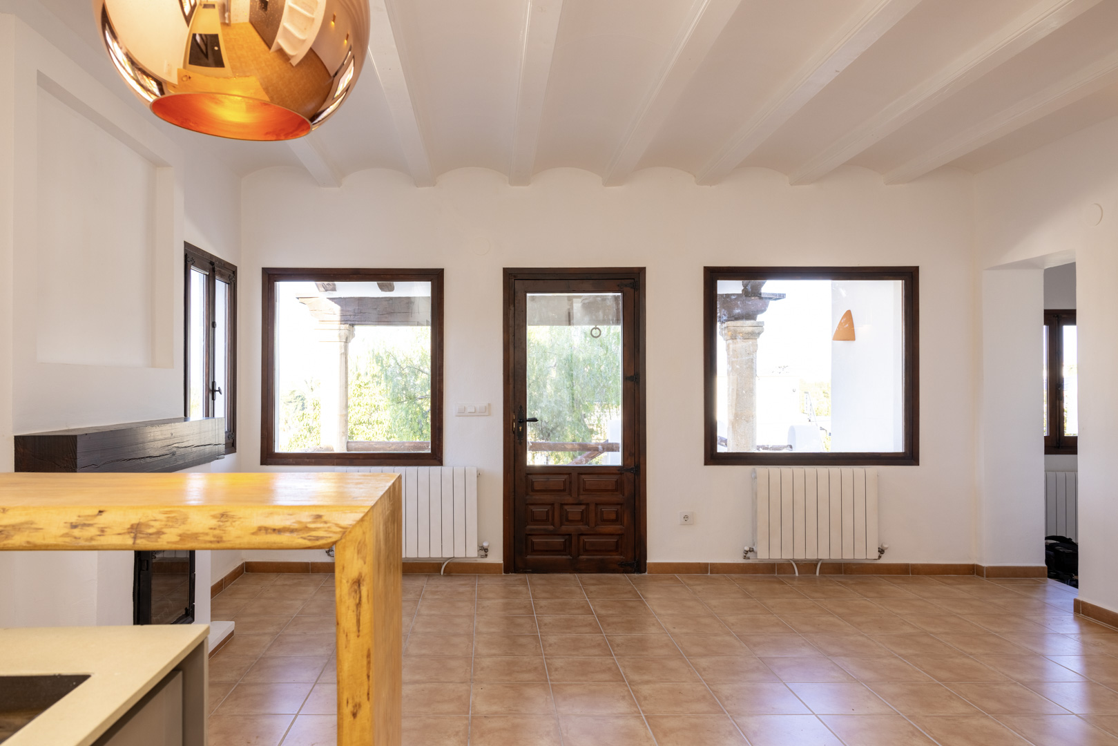 Bright living room with tile floor, exposed beams, and dark wood trim. Views to the outside.