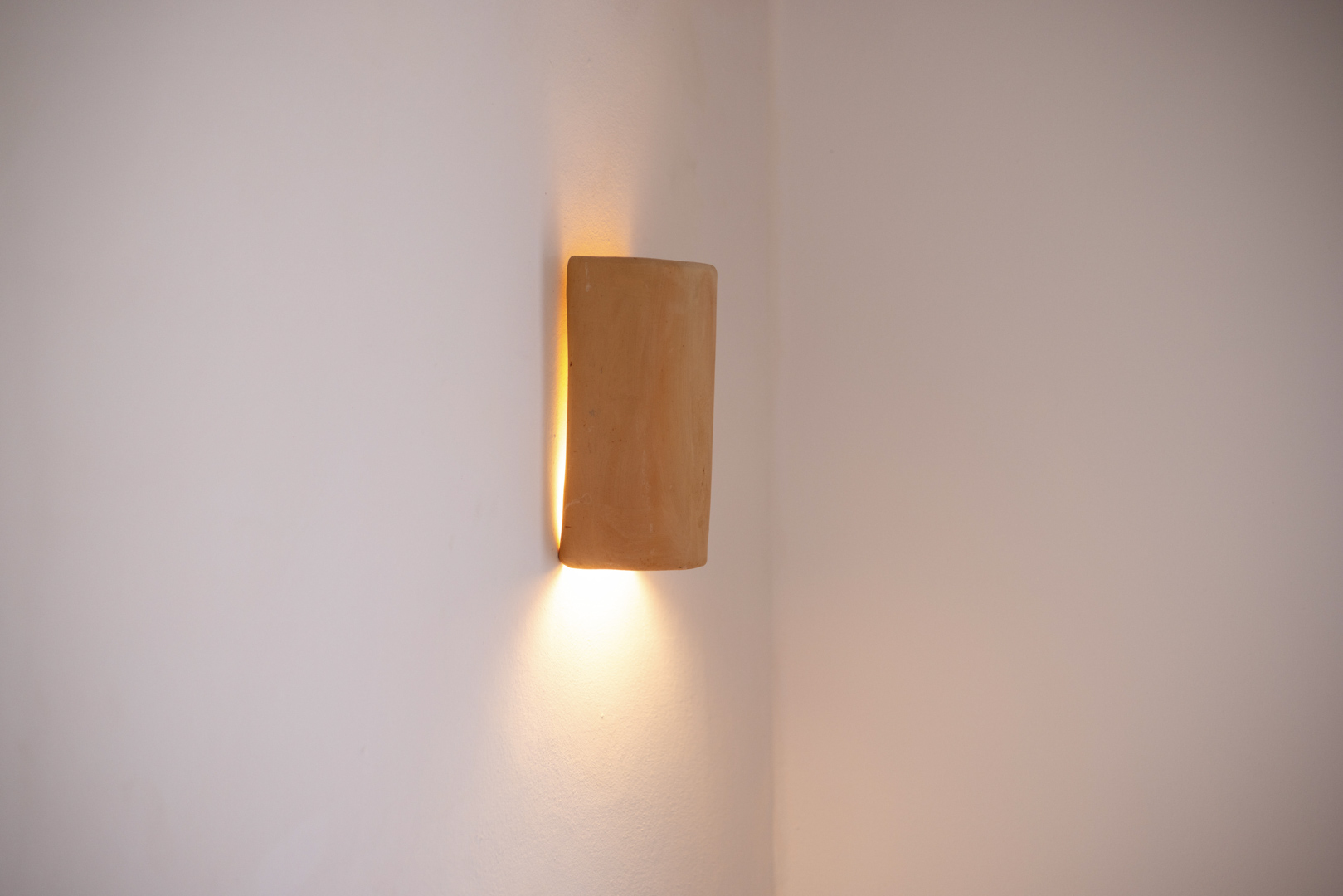 Close-up of a rustic wall sconce, casting a warm glow in a minimalist interior.