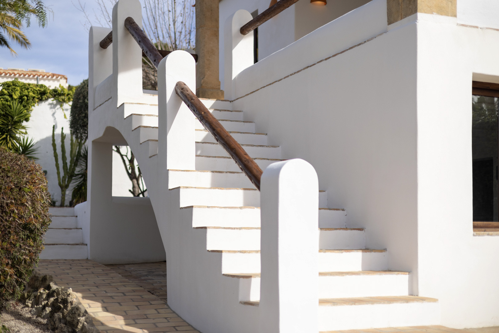 Detail of white exterior staircase with wooden railing and brick paving.