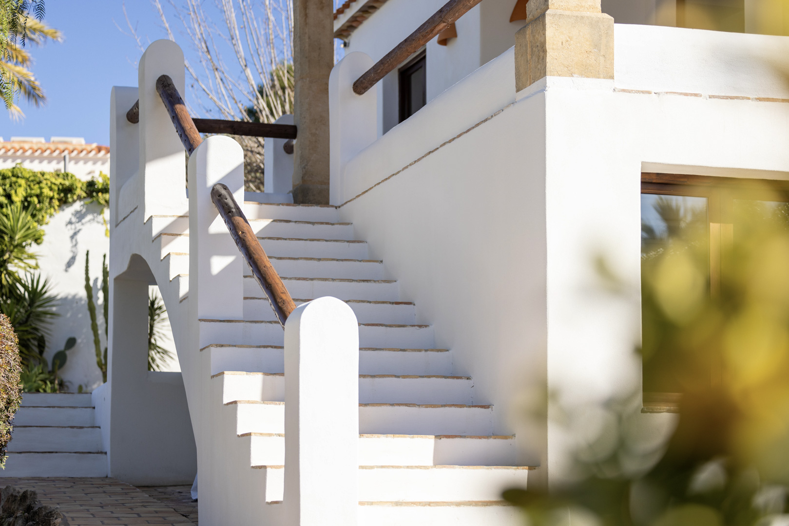 Detail of white exterior staircase with wooden railing at Jávea villa. Bright Mediterranean design.