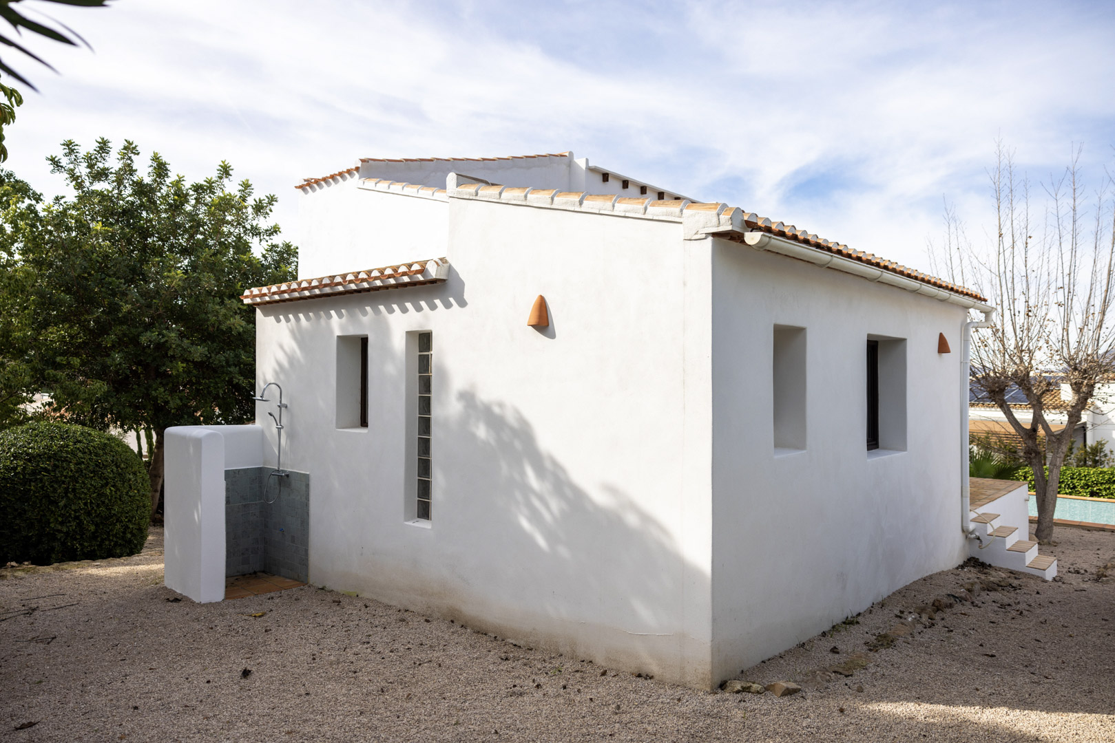 Exterior view of the villa showcasing the tiled outdoor shower and minimalist white facade with windows.