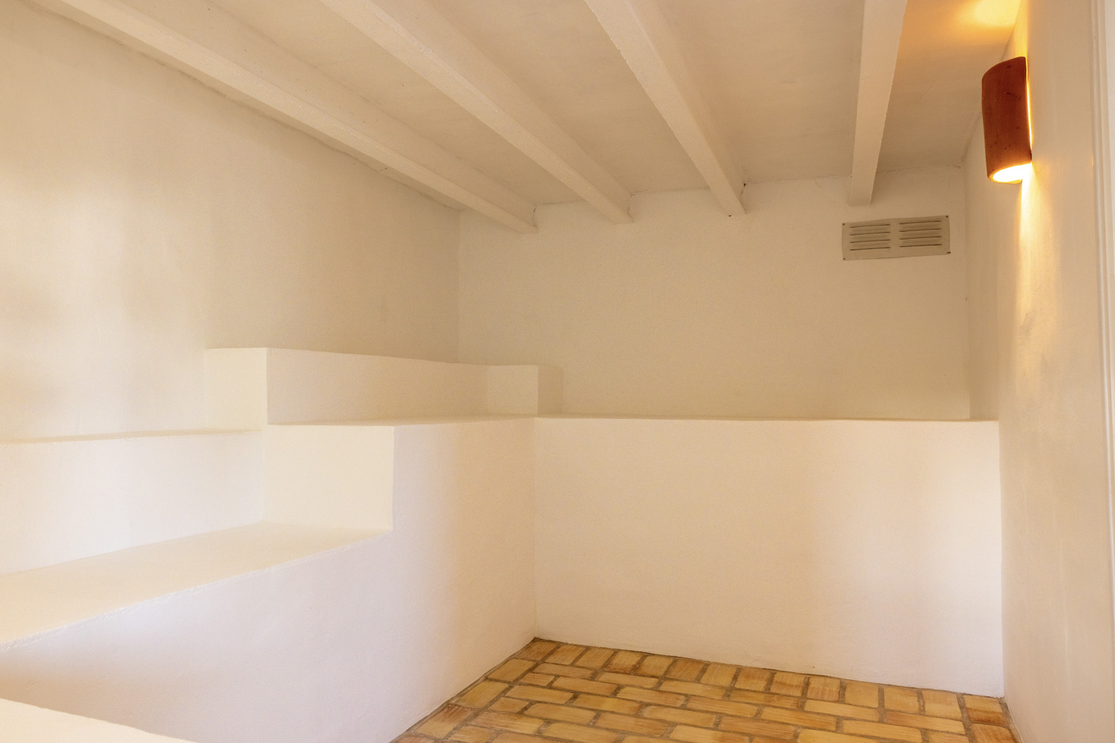Interior detail with brick floor, white walls, and warm light. Exposed beams on the ceiling.
