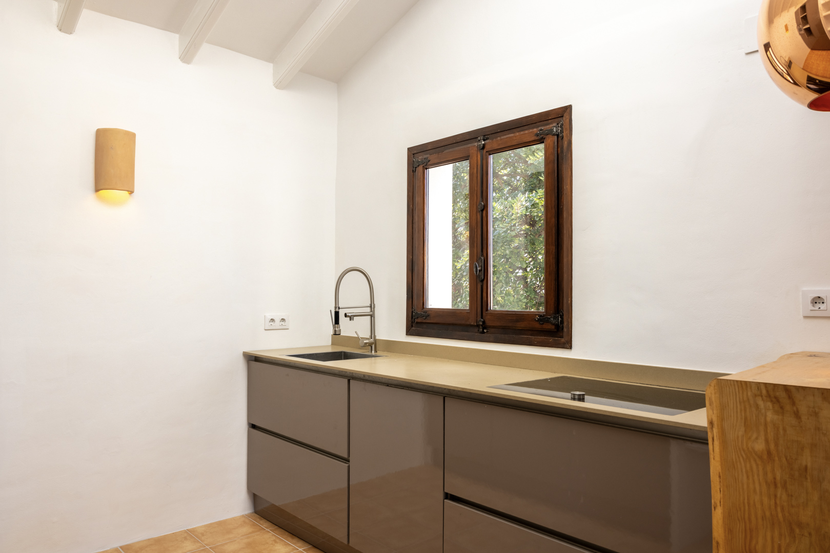 Kitchen detail with beige countertop, steel sink, and wooden window overlooking the exterior.