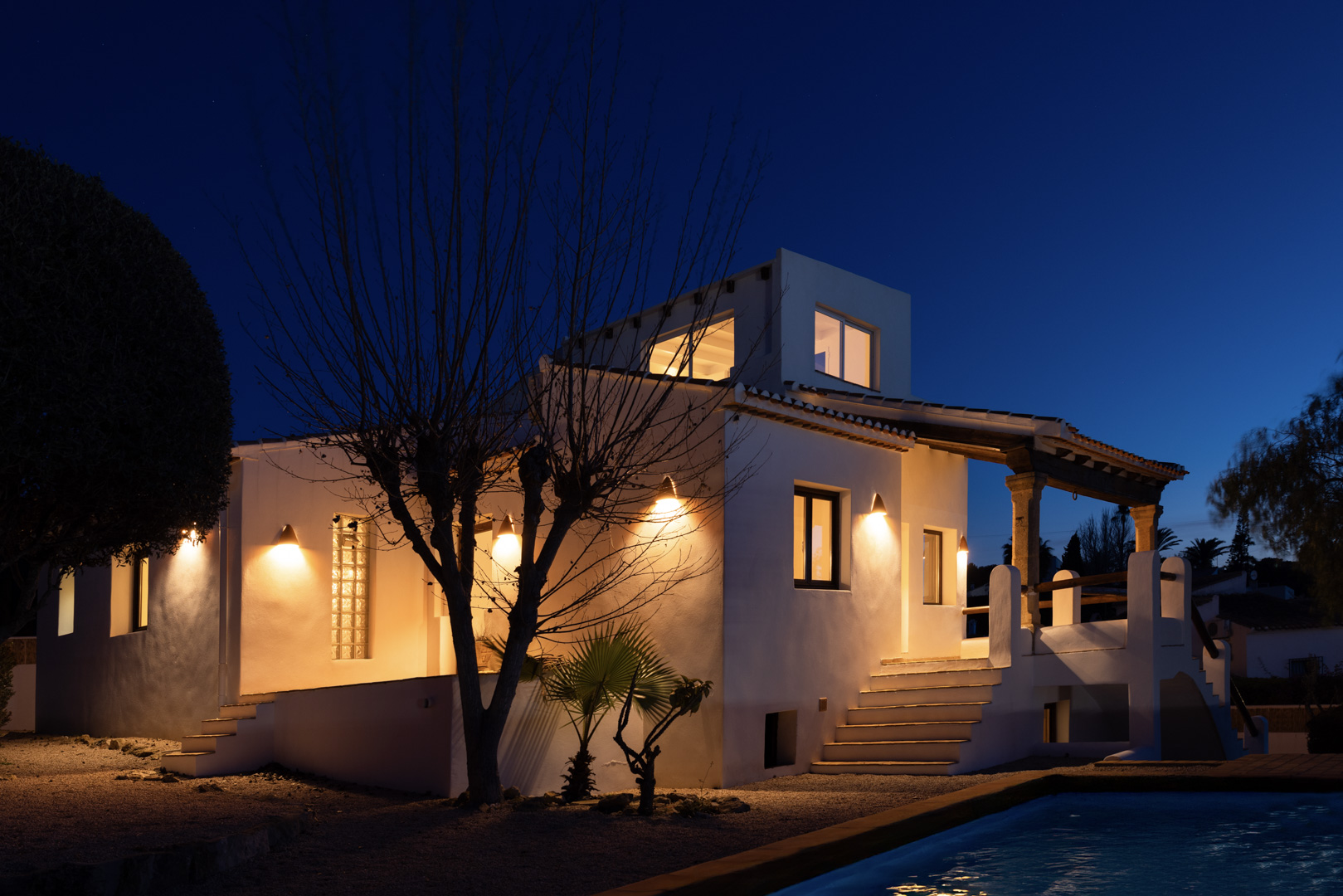 Night view of the illuminated villa featuring a reflective pool and traditional white facade.