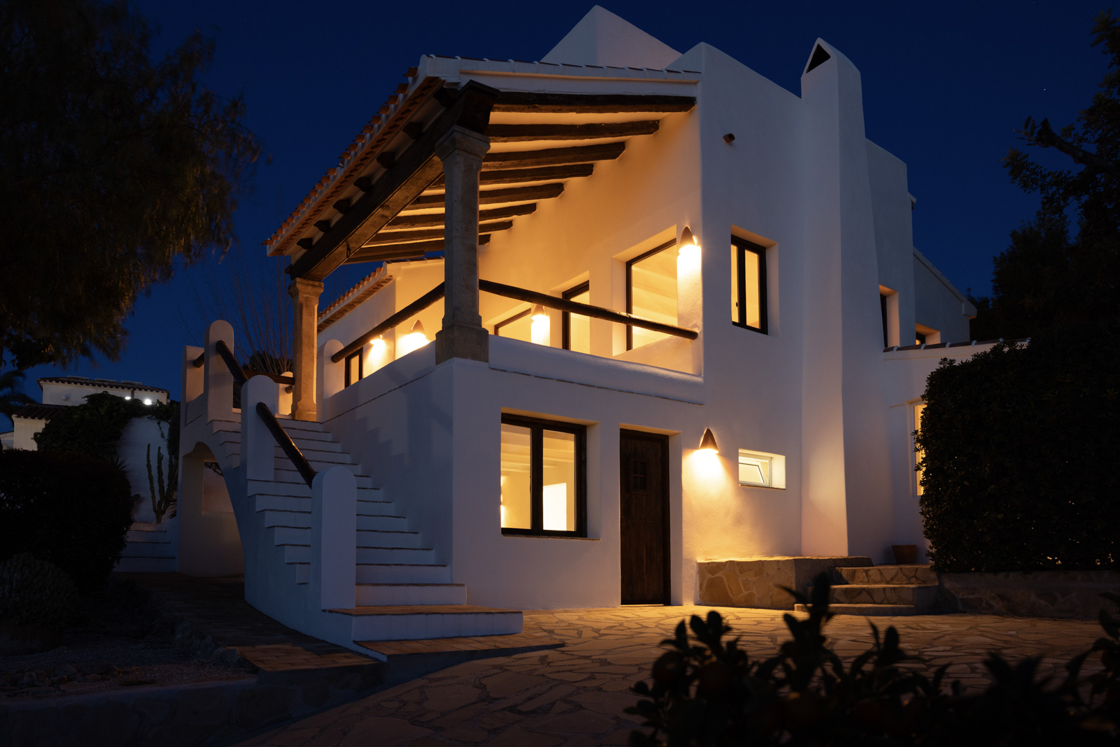 Night view of the villa featuring a lit, covered terrace and exterior stone staircase.