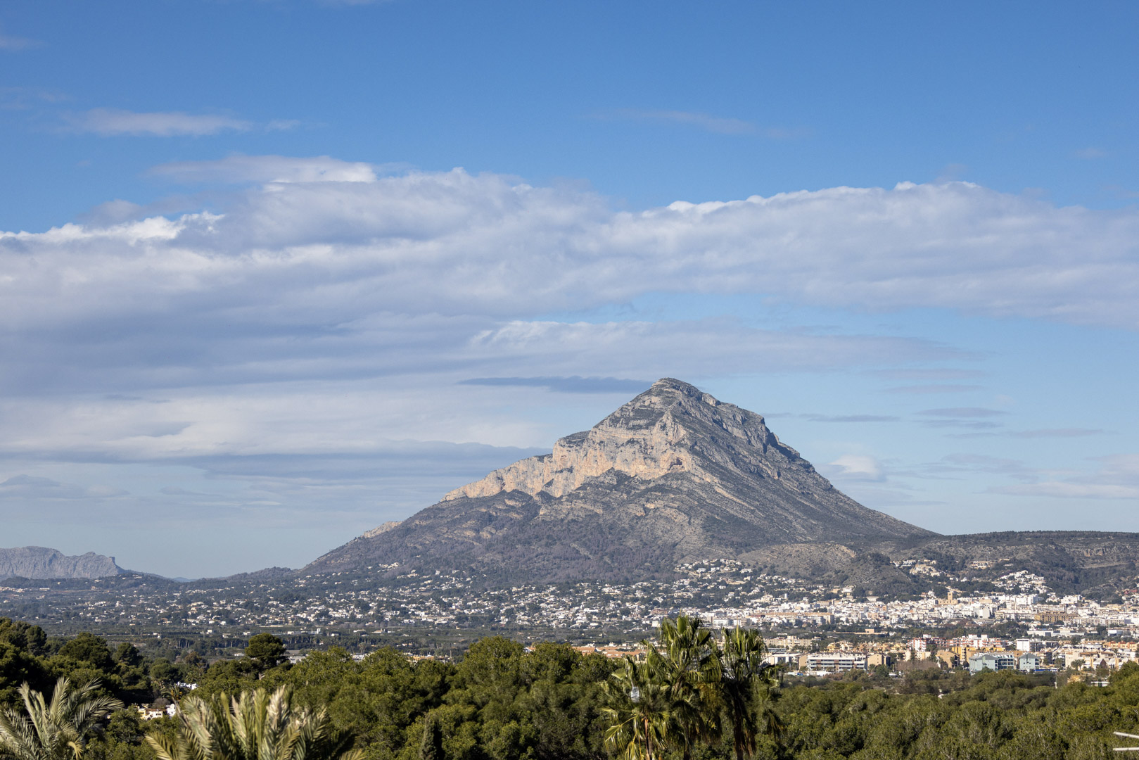 Panoramic view of Montgó, Jávea, with a partly cloudy sky and vegetation in the foreground.