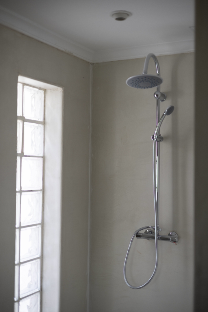 Shower detail with rainfall head and glass block window in a bathroom with cream-colored walls.