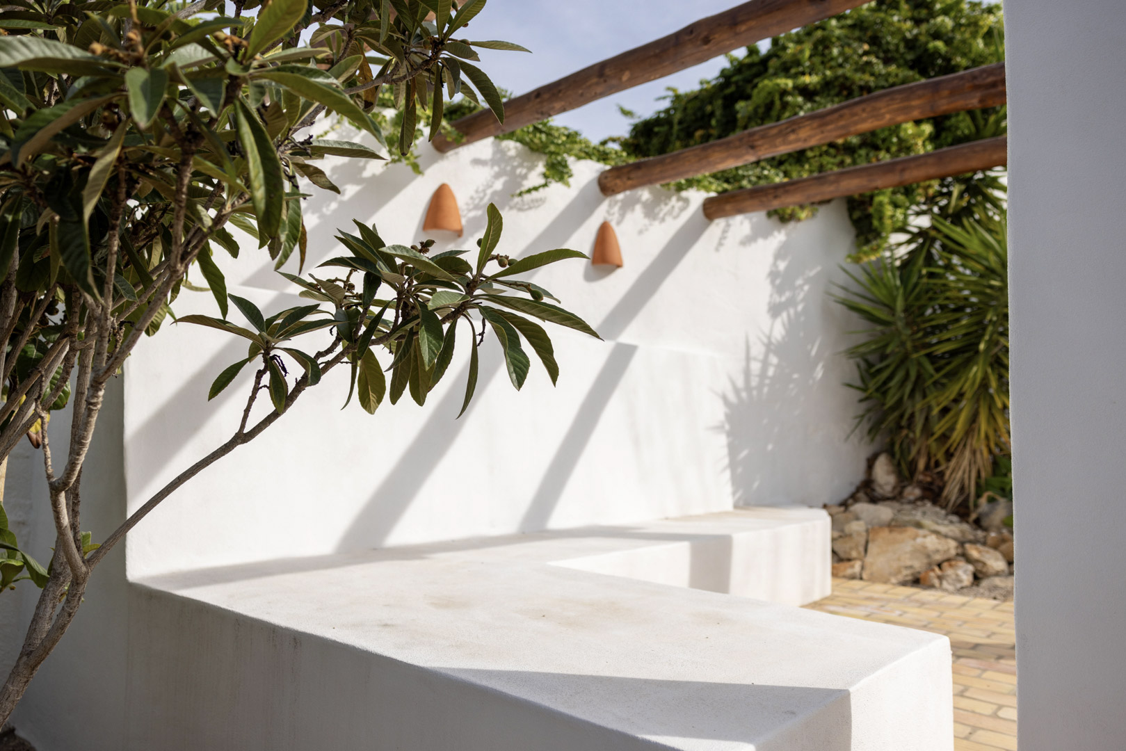 Terrace detail with whitewashed concrete bench, wooden pergola, and lush greenery.