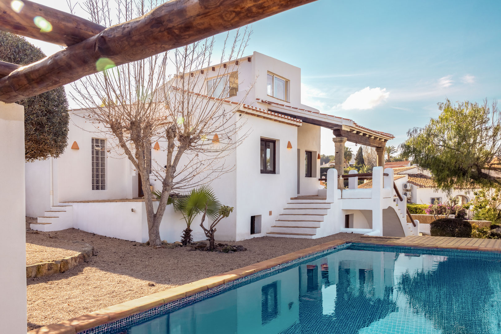 View of the villa with turquoise blue pool and white facade. Mediterranean design with gravel garden.