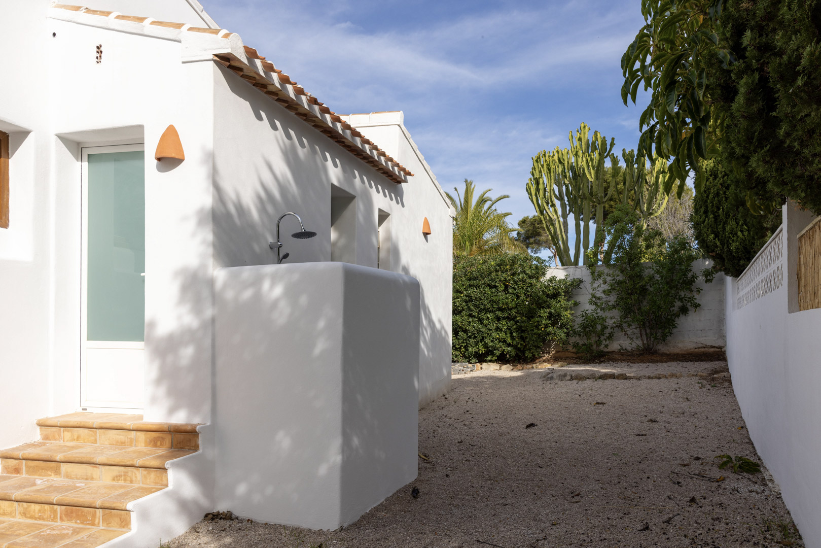 Villa exterior featuring an outdoor shower and gravel garden with varied greenery.