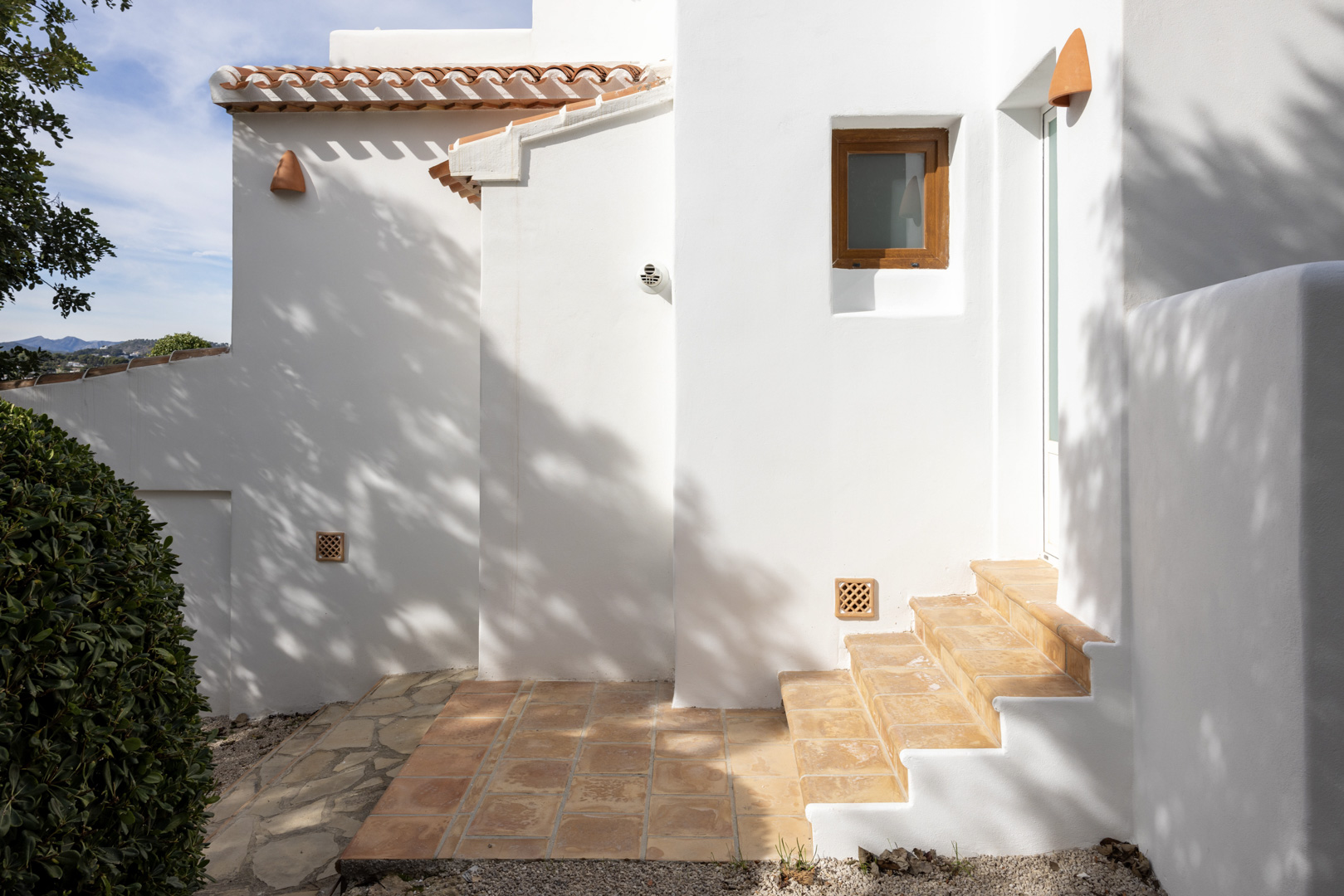 Villa exterior in Jávea featuring white walls, terracotta roof tiles, and access stairs.