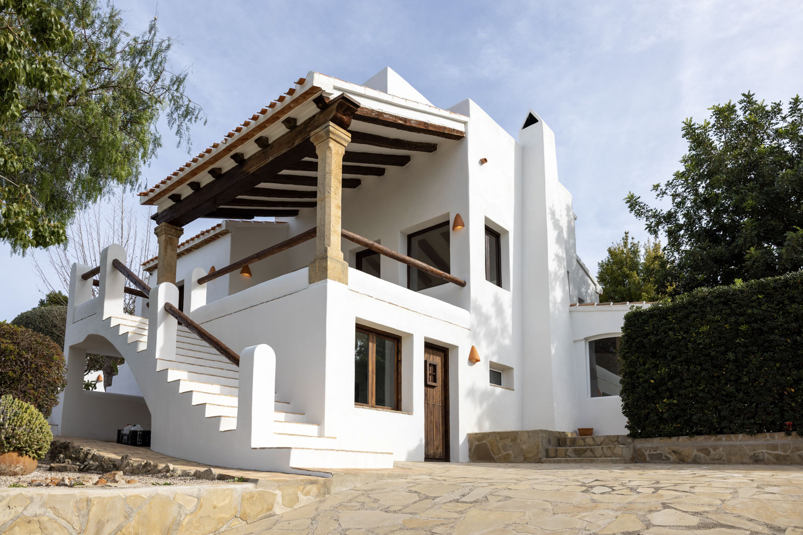 Villa facade in Jávea featuring a covered terrace, stone columns, and access via outdoor stairs.
