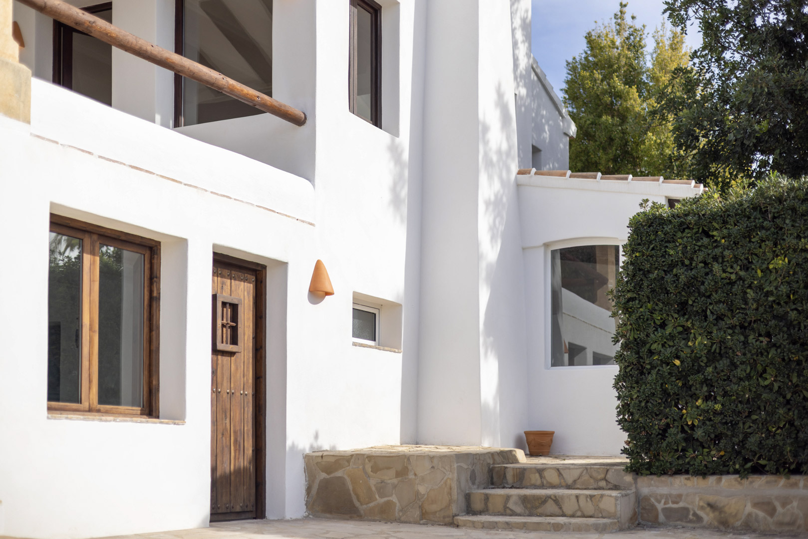 Villa facade in Jávea featuring rustic details: wood door, white walls, and stone steps.