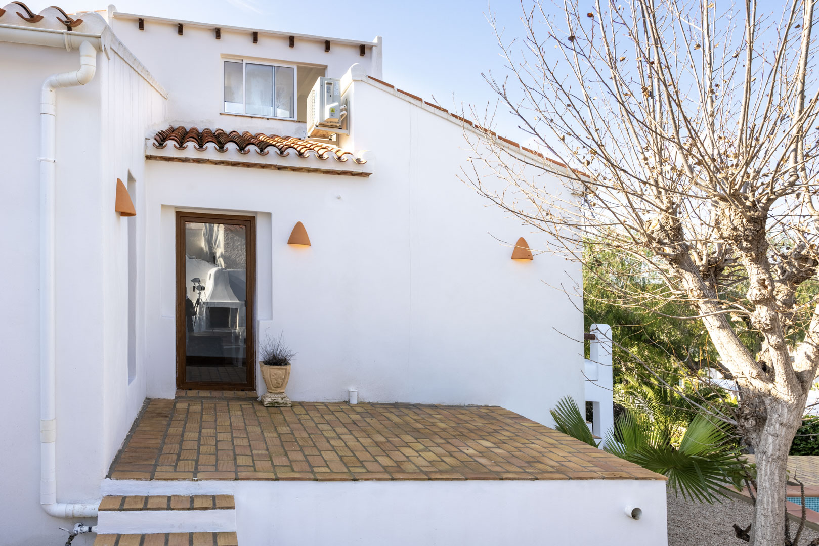 White facade with brick terrace and rustic lighting details.