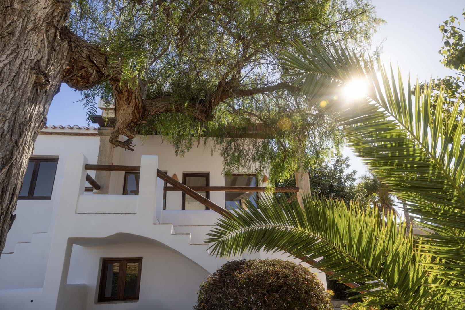 White facade with wooden balcony and lush greenery, highlighting the Mediterranean architecture.