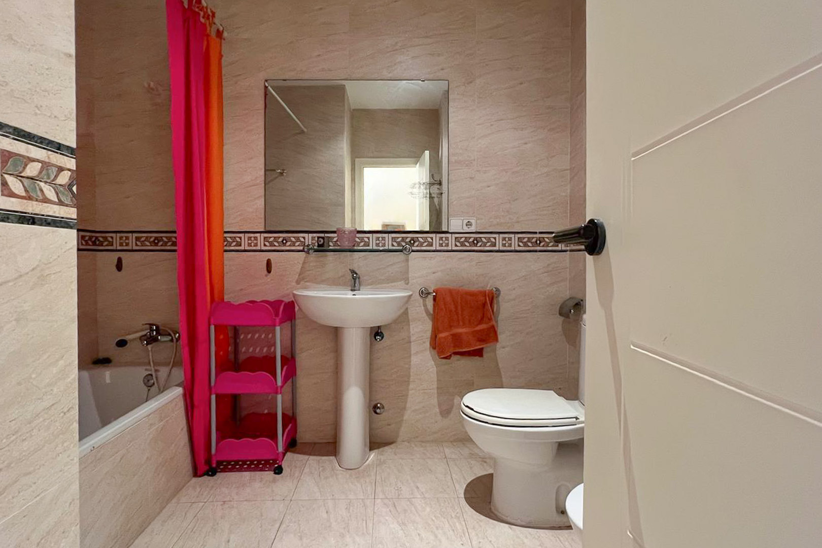 Bathroom featuring cream-colored tiles, a white pedestal sink, and decorative wall accents.