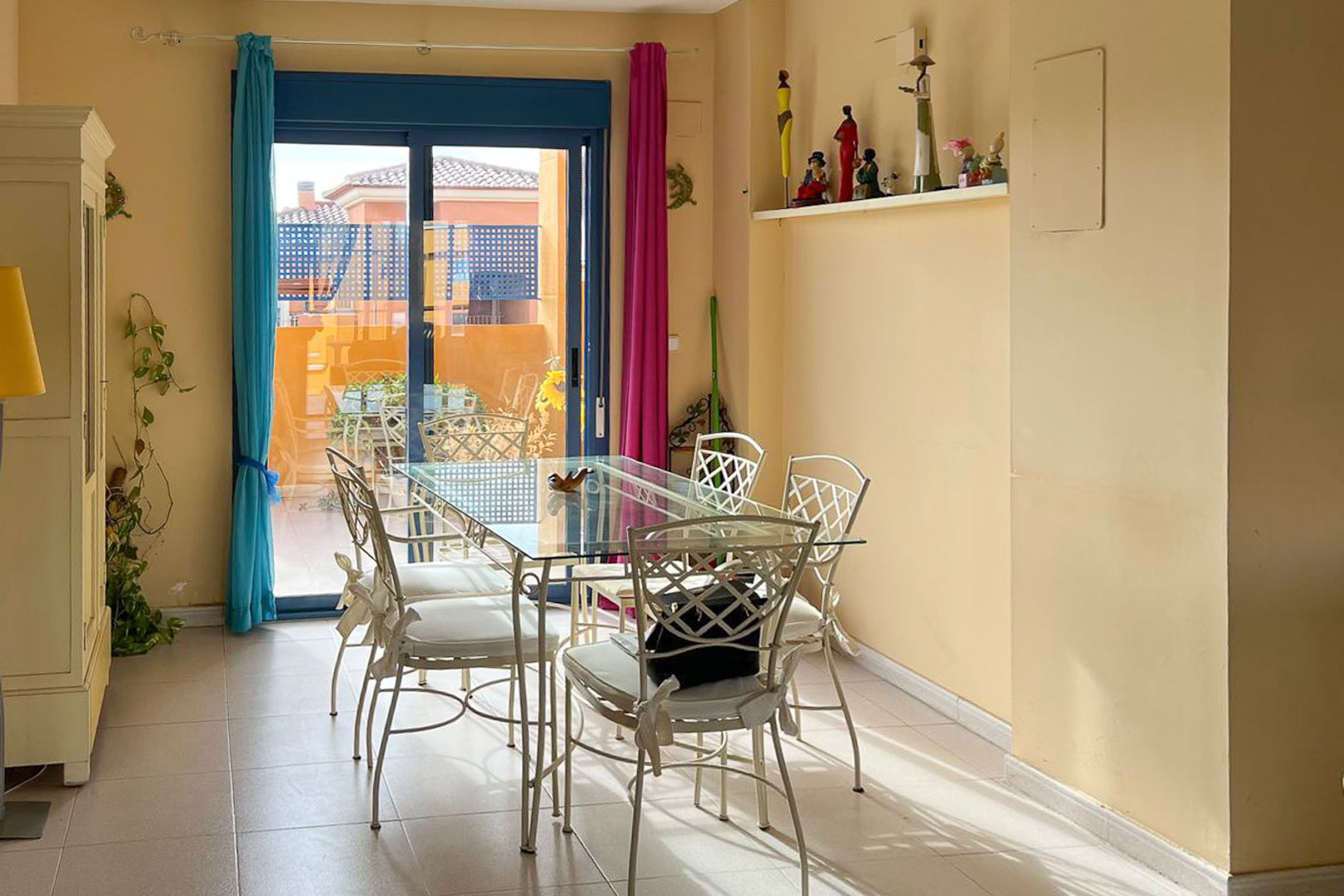 Bright dining room with a glass table and wrought iron chairs, accessing a terrace with views.