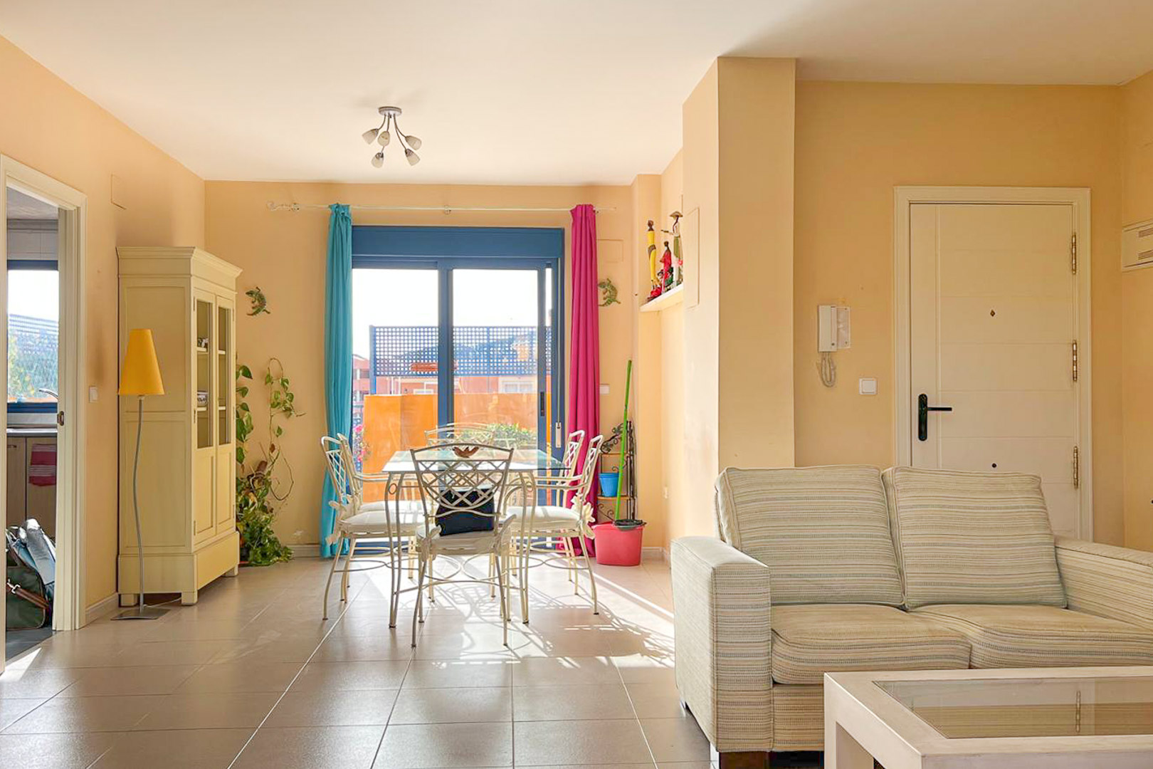 Bright living-dining room with balcony, metal dining table and neutral striped sofa.