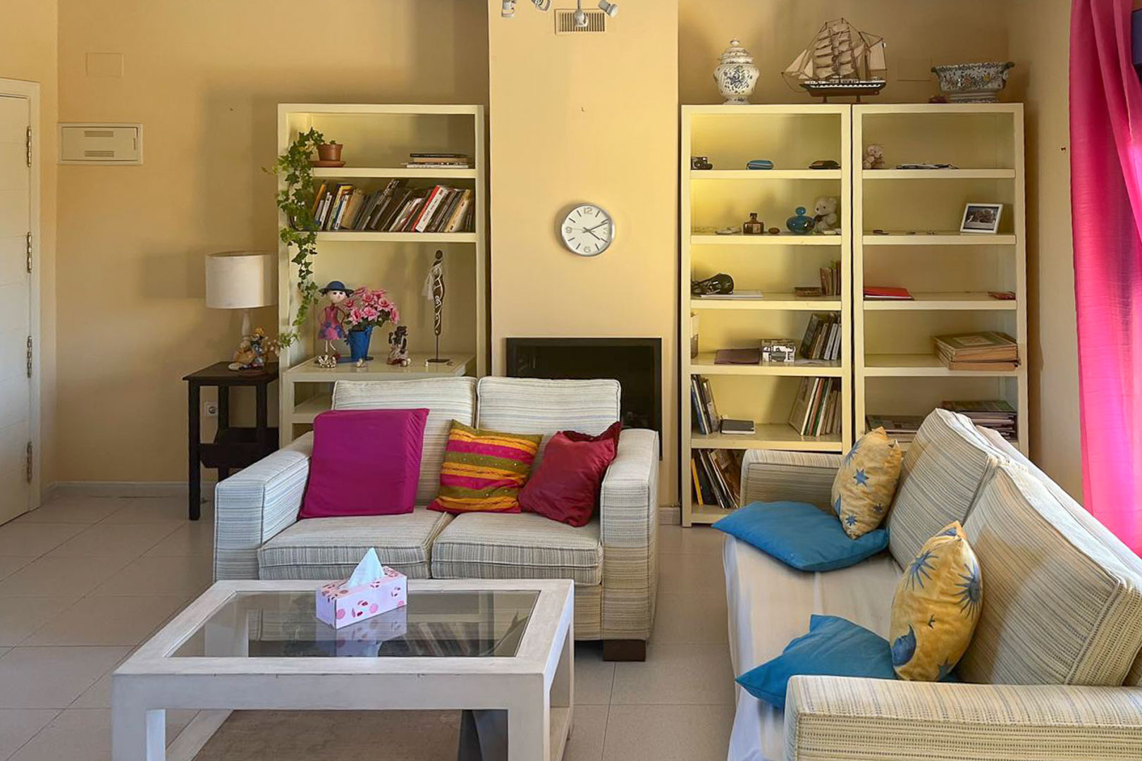 Bright living room featuring cream bookshelves, striped sofas, and a glass coffee table.