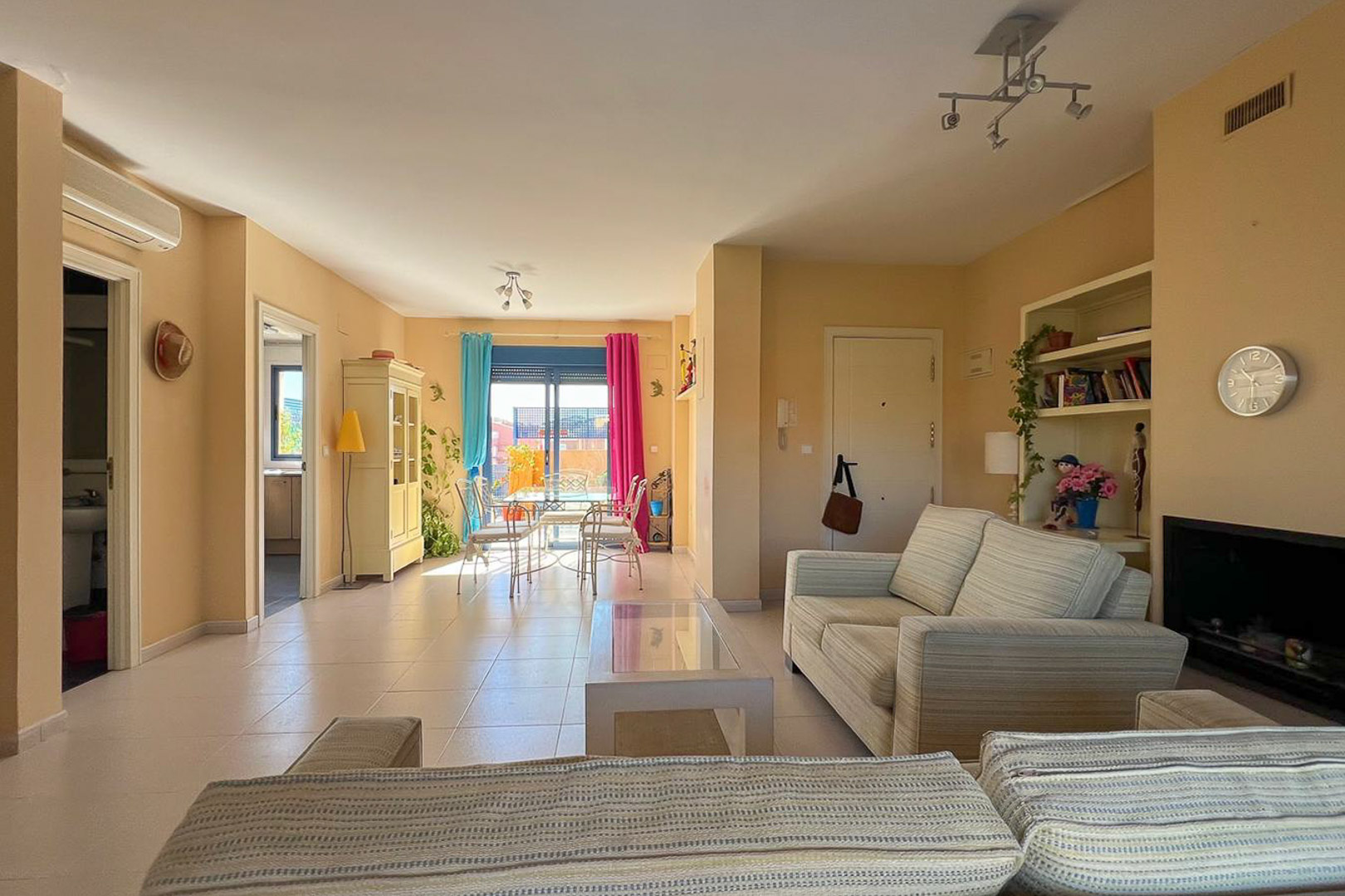 Bright living room with upholstered sofas and access to a terrace with colorful curtains.