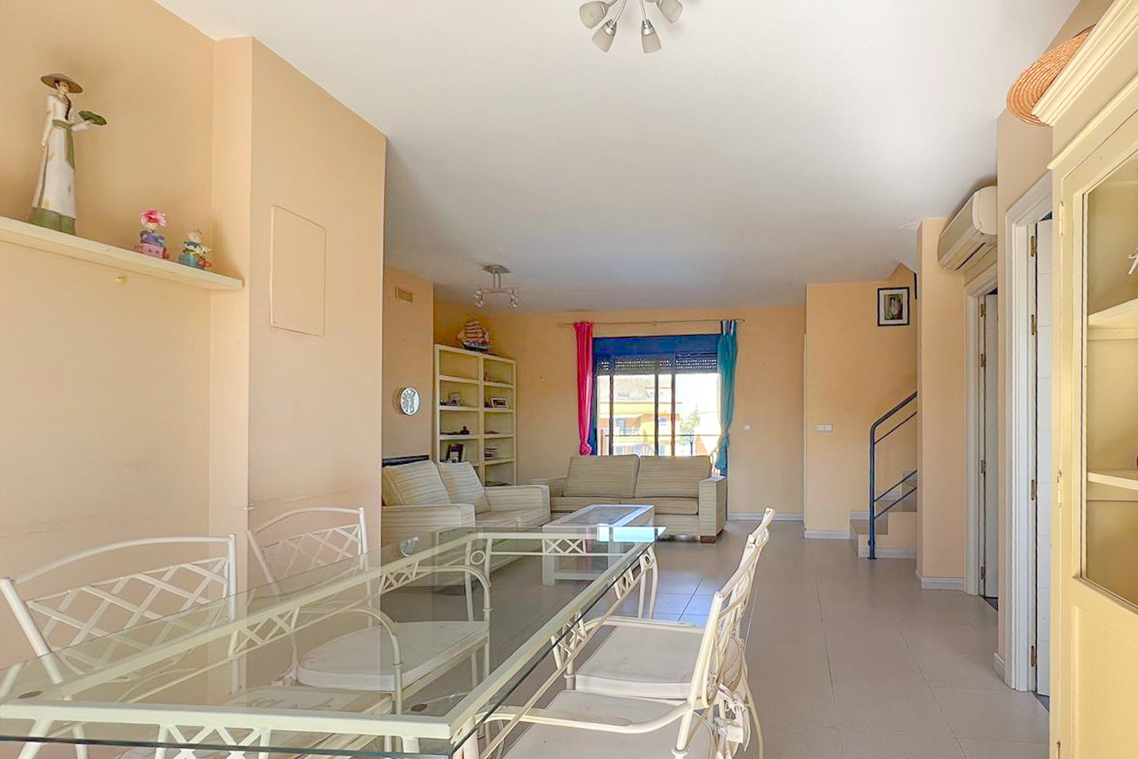 Living-dining area featuring a glass table, striped sofas, and a bookshelf with nautical decor.