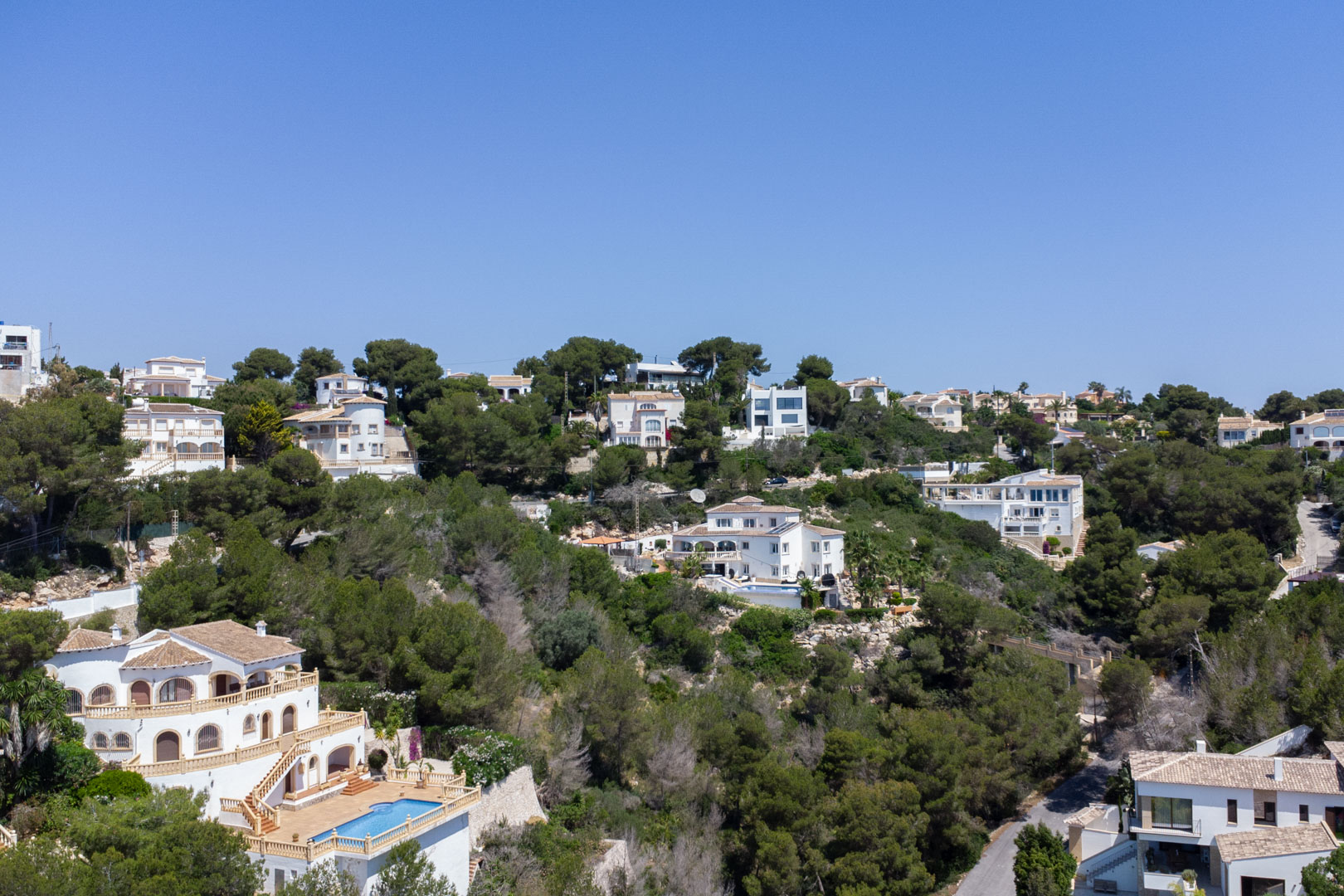 Elevated view of the Costa Nova residential area in Jávea, featuring Mediterranean villas with private pools nestled among pine-covered hillsides.