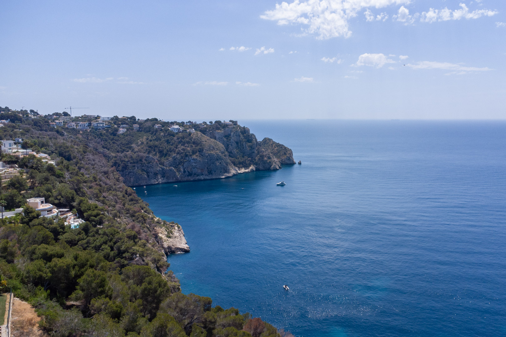 Elevated view of the Granadella coastline in Jávea, featuring rugged cliffs, Mediterranean pine forests, and expansive views of the deep blue sea.