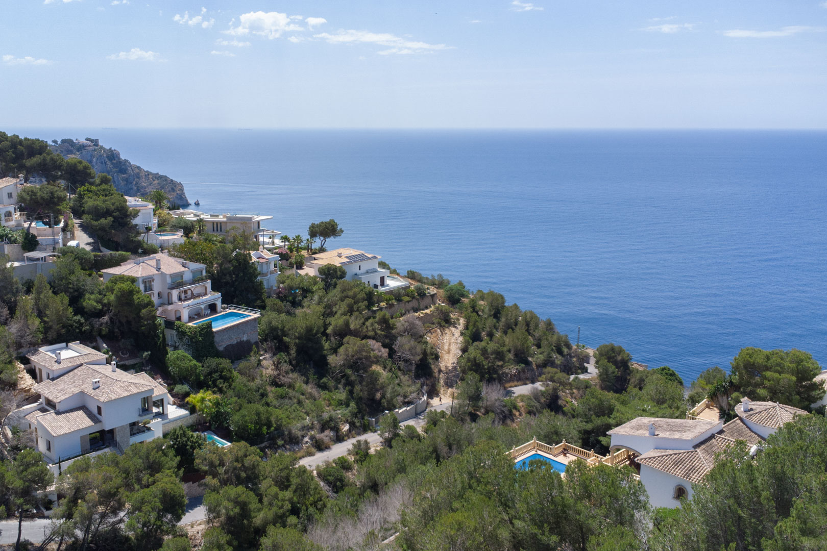 Elevated view of the Jávea coastline featuring Mediterranean villas nestled in pine forests with expansive views of the deep blue sea.