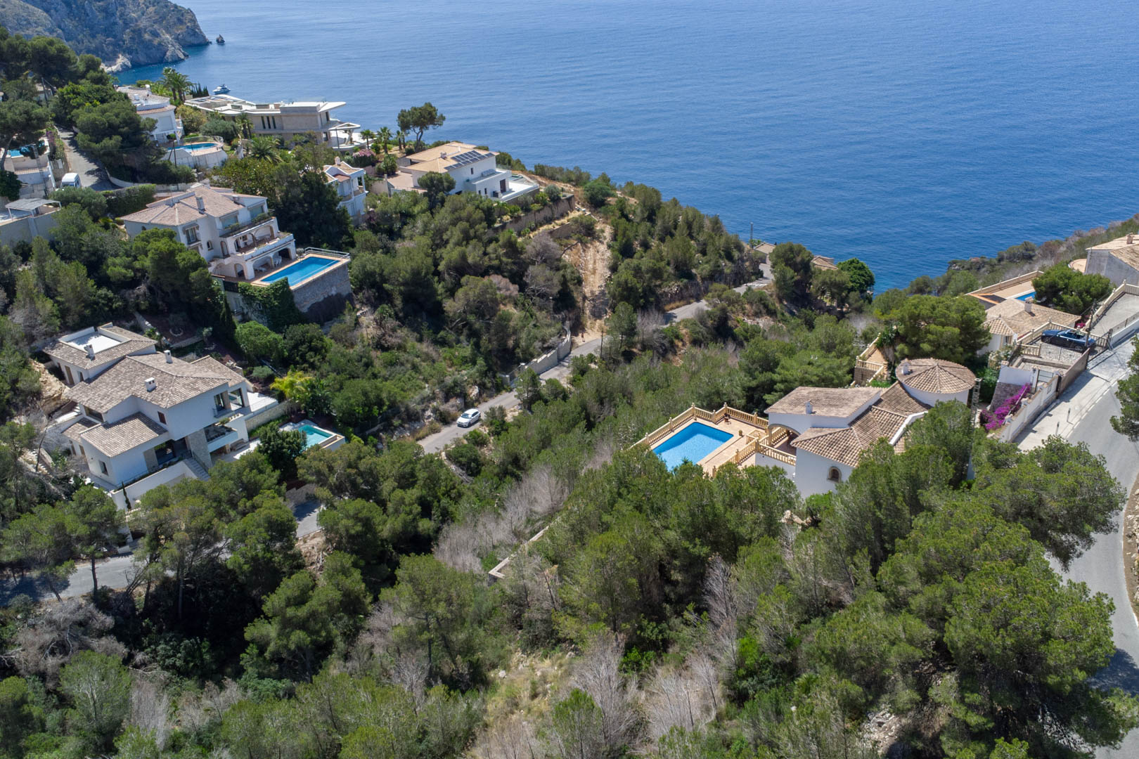 Aerial view of residential plots in Costa Nova, Jávea, featuring Mediterranean pine forests, luxury villas with pools, and expansive sea views.