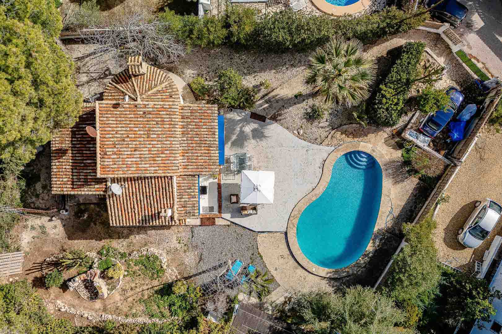 Aerial bird's-eye view of the property showcasing the kidney-shaped pool, paved sun terrace, and traditional terracotta roof within the private plot.