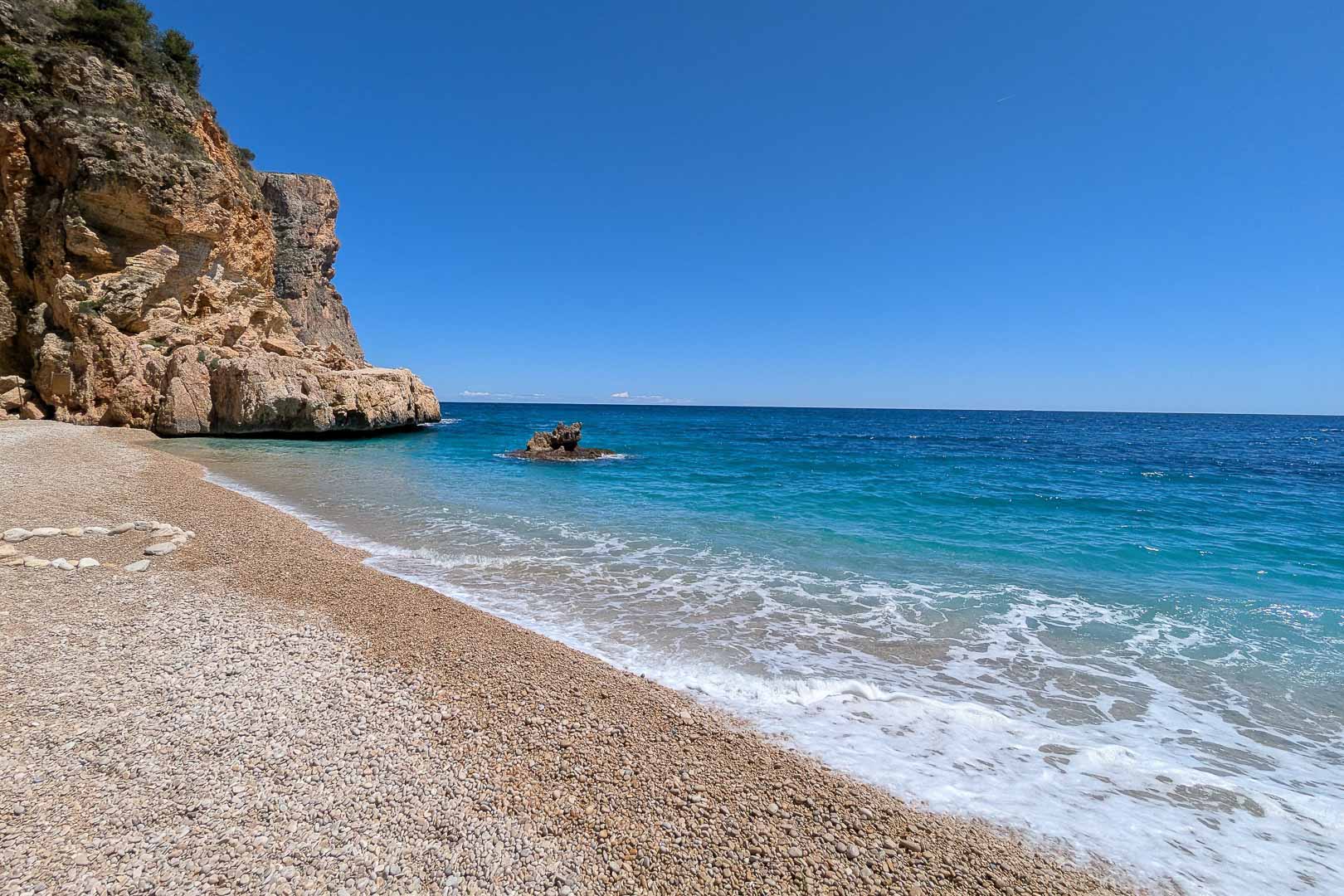 Cala Llebeig, a secluded pebble cove with turquoise waters and limestone cliffs, located within walking distance from the property in Moraira.