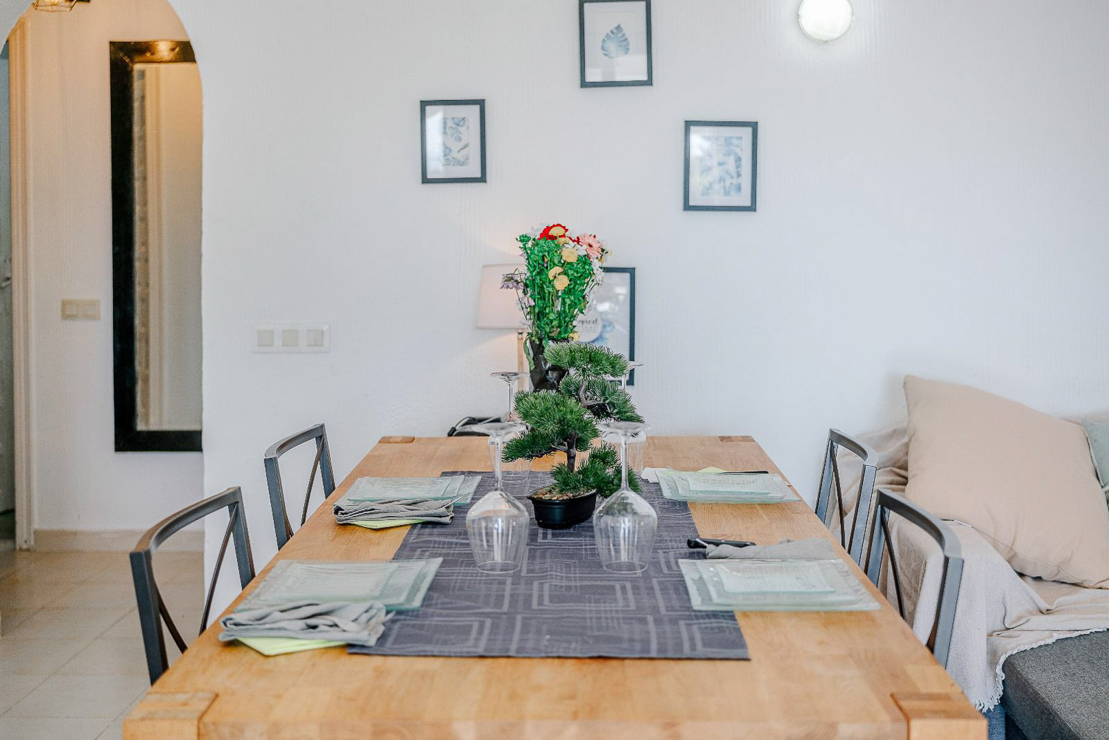 Dining area featuring a light wood table and metal chairs, styled with a botanical centerpiece and wall art beside a classic arched doorway.
