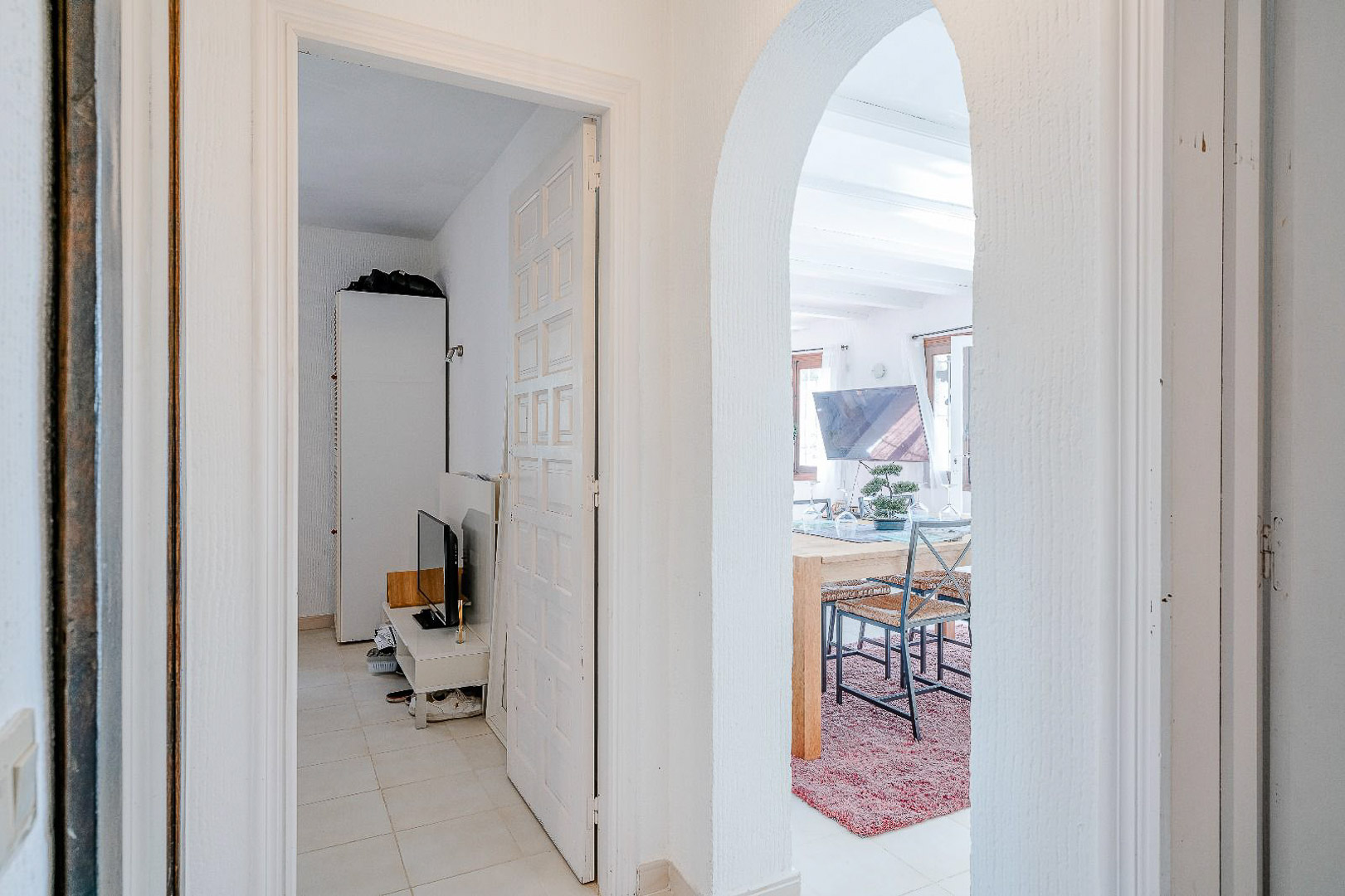 Distribution hallway featuring a Mediterranean archway leading to the dining room and a white paneled door opening into a bright bedroom.