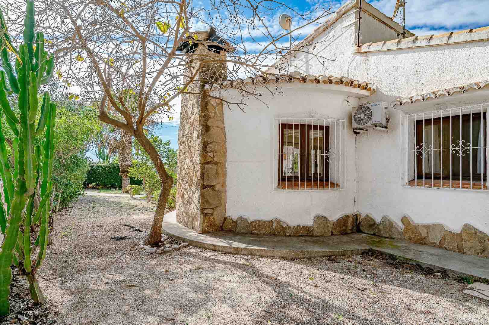 Mediterranean exterior featuring a white facade with natural stone cladding, wooden windows with white security bars, and a gravel garden with native cacti.