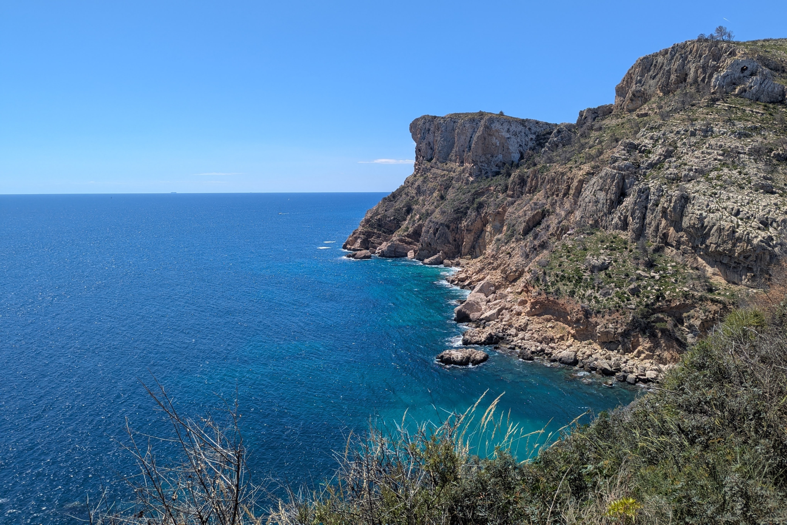 Panoramic views of the rugged limestone cliffs and turquoise Mediterranean waters near Cala Llebeig, framed by native coastal vegetation.