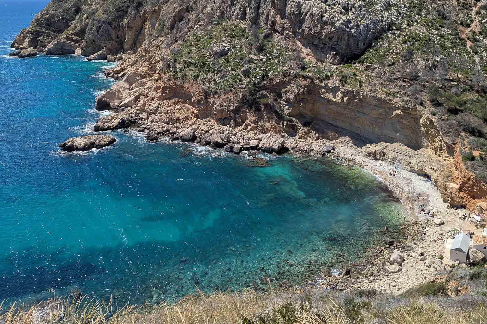 View of Cala Llebeig featuring crystal-clear turquoise waters and rugged cliffs, accessible via a trail near the rear of the property.