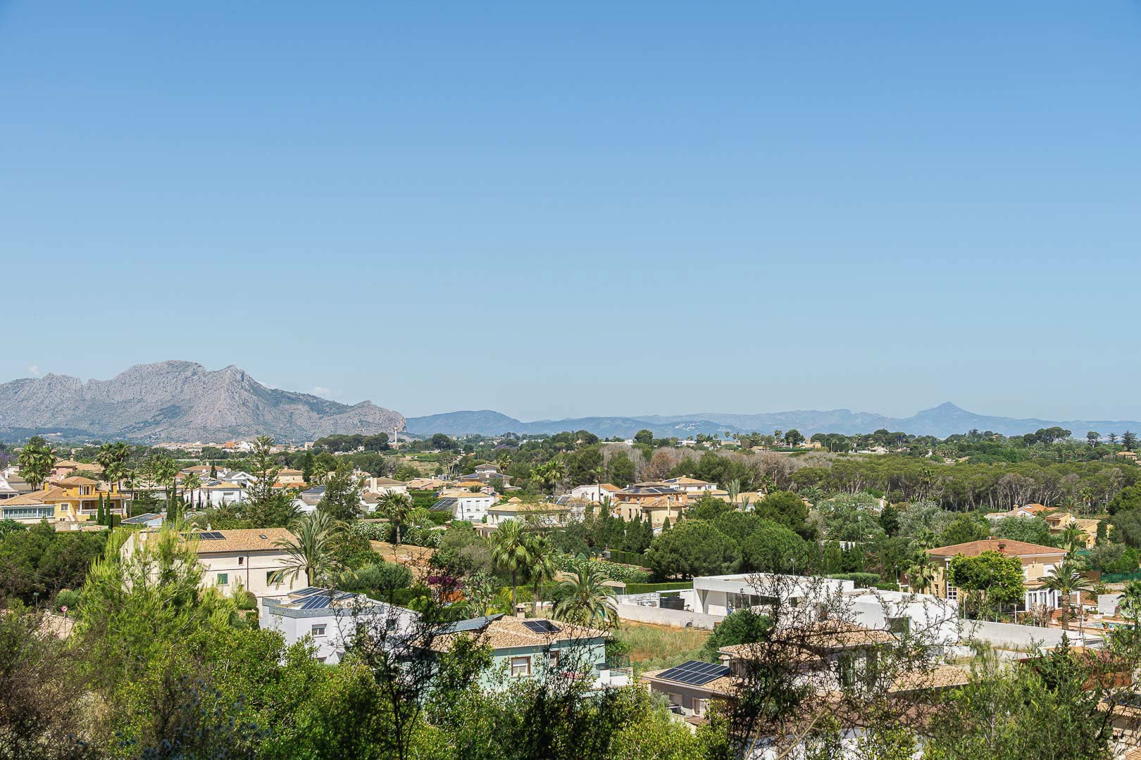 Panoramic view of Dénia featuring homes, greenery, and mountains in the background.
