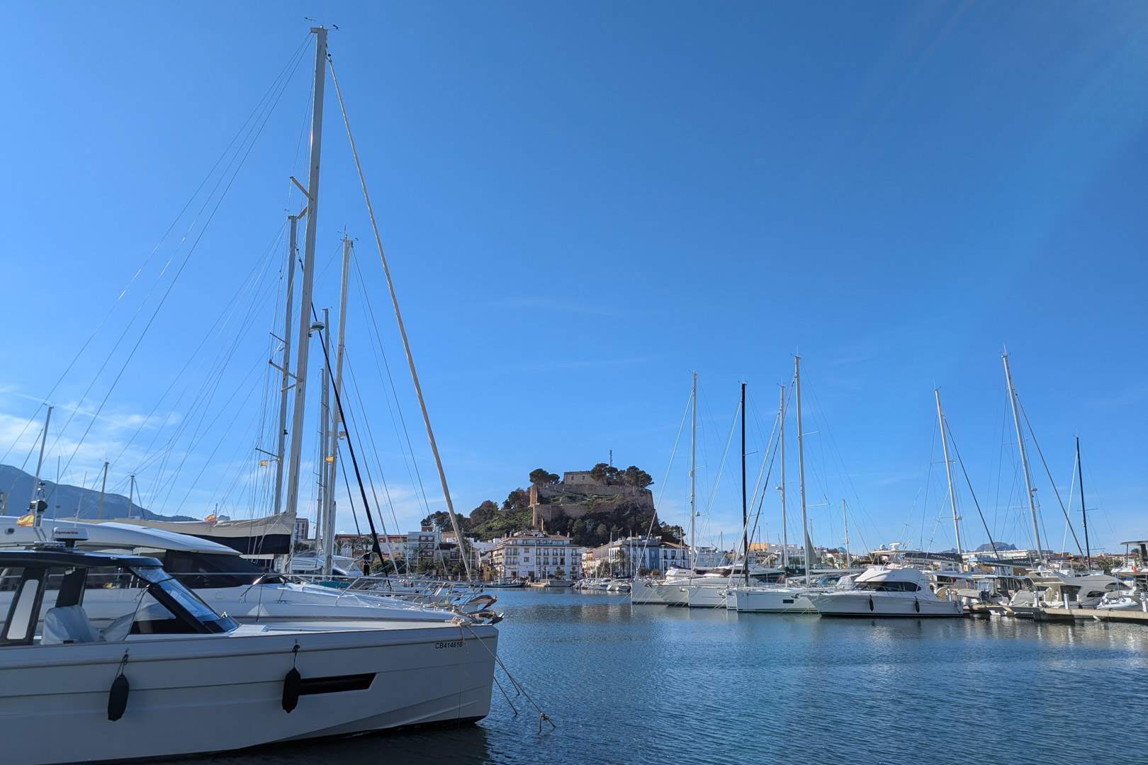 View of the marina with yachts and the Dénia castle in the background under a clear blue sky.