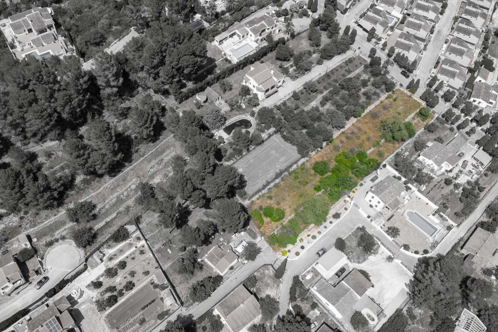 Aerial view of Residencial VALL DE POP in Alcalalí, showing the highlighted green plots within a developed neighborhood featuring mature trees and a nearby tennis court.