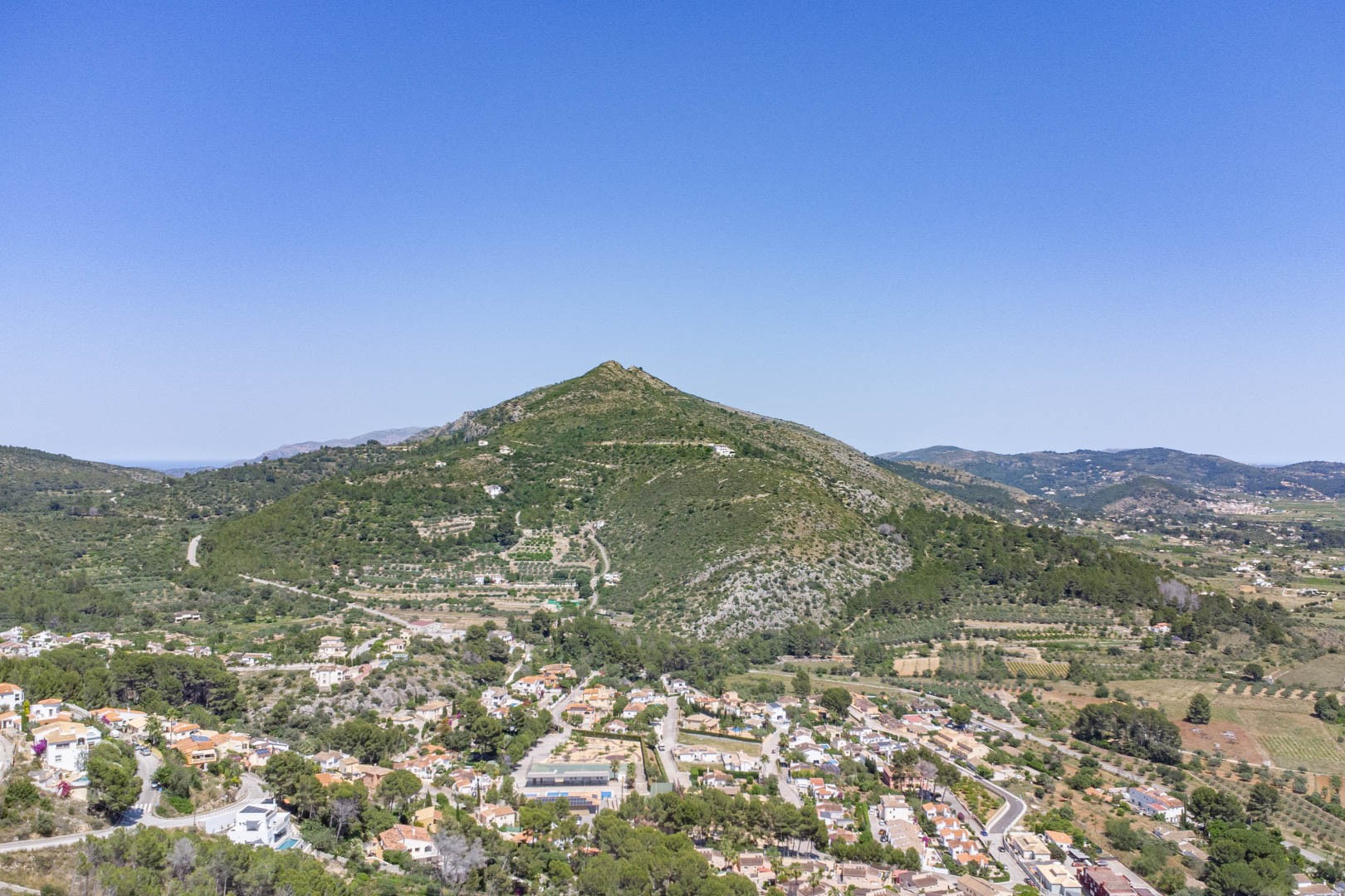 Panoramic aerial view of Alcalalí village and the Jalón Valley, showcasing the Mediterranean mountain landscape and the residential integration within the natural surroundings.