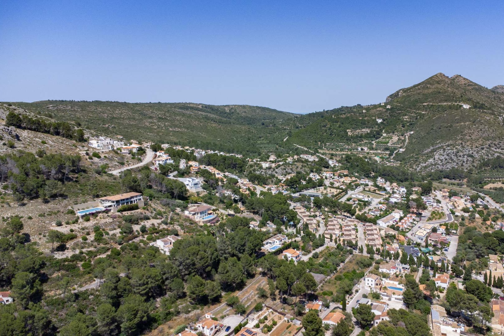 Panoramic aerial view of the VALL DE POP residential area in Alcalalí, highlighting the elevated plots integrated into the lush Mediterranean valley landscape.